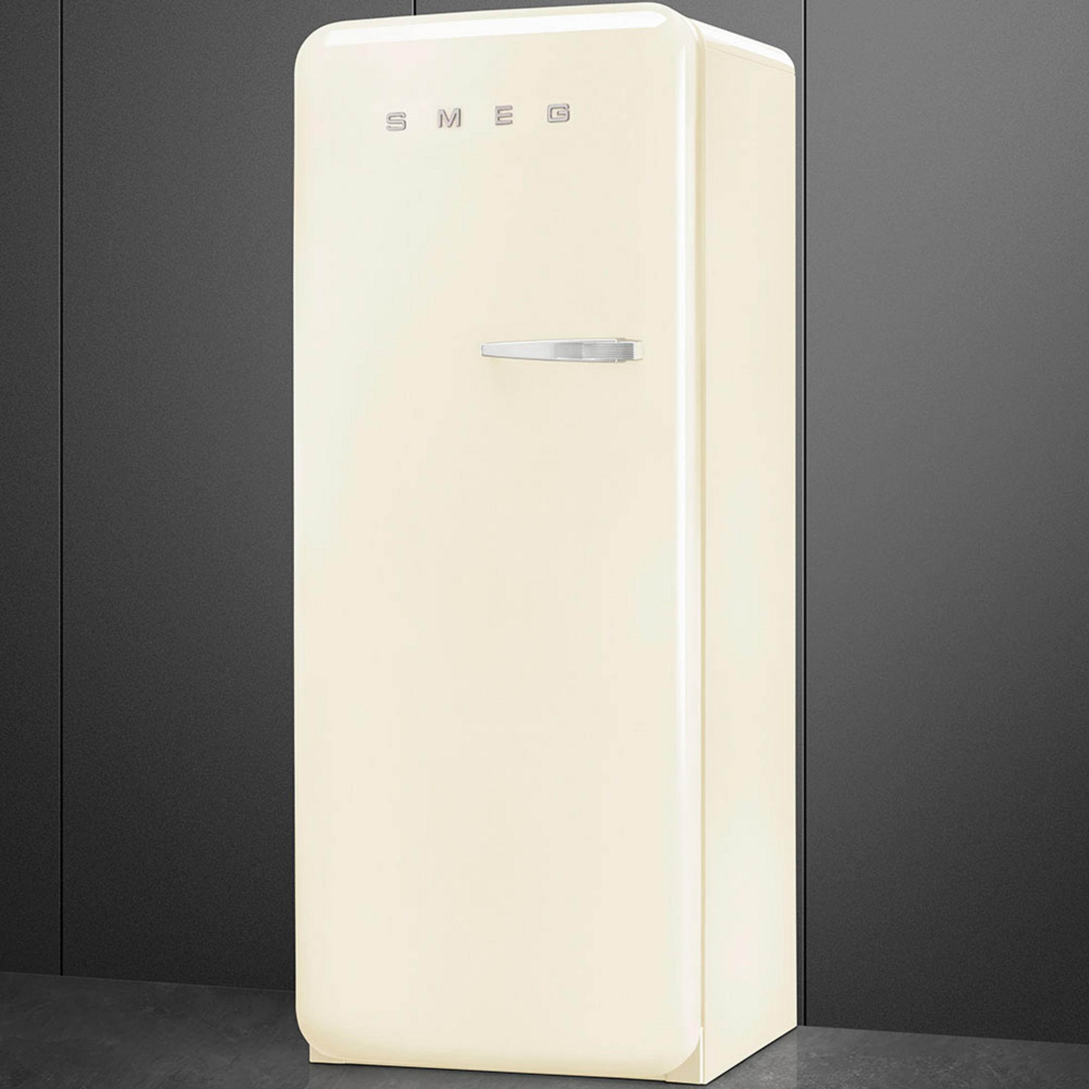 Ein cremefarbener Smeg-Kühlschrank mit silbernem Griff vor einer dunklen Wand.