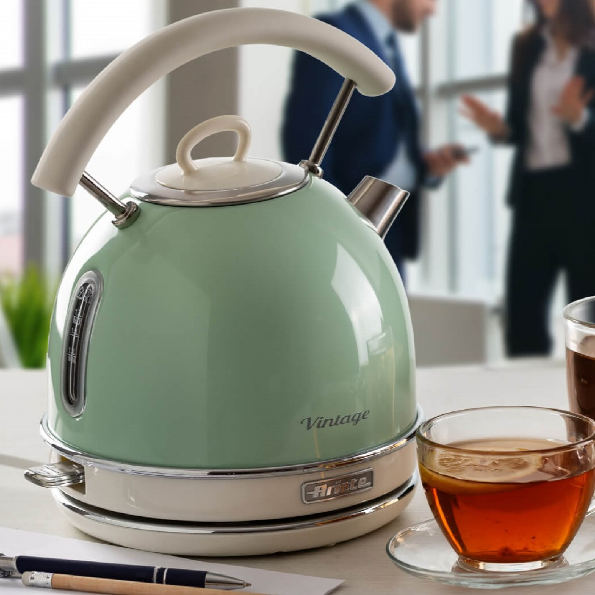 Een mintgroene waterkoker met witte handgreep naast een kop thee.