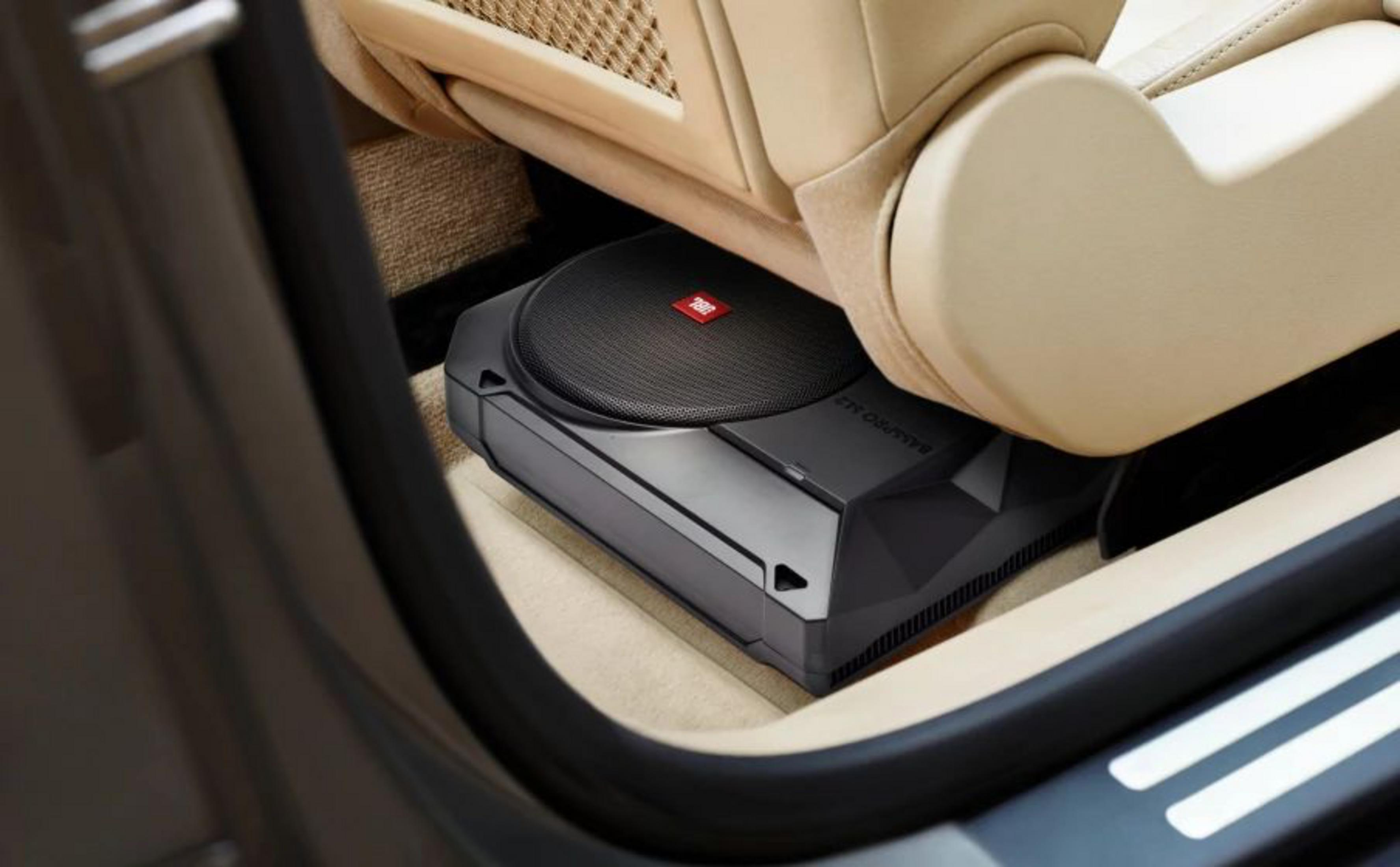 Ein schwarzer Subwoofer mit JBL-Logo unter einem beigen Autositz.