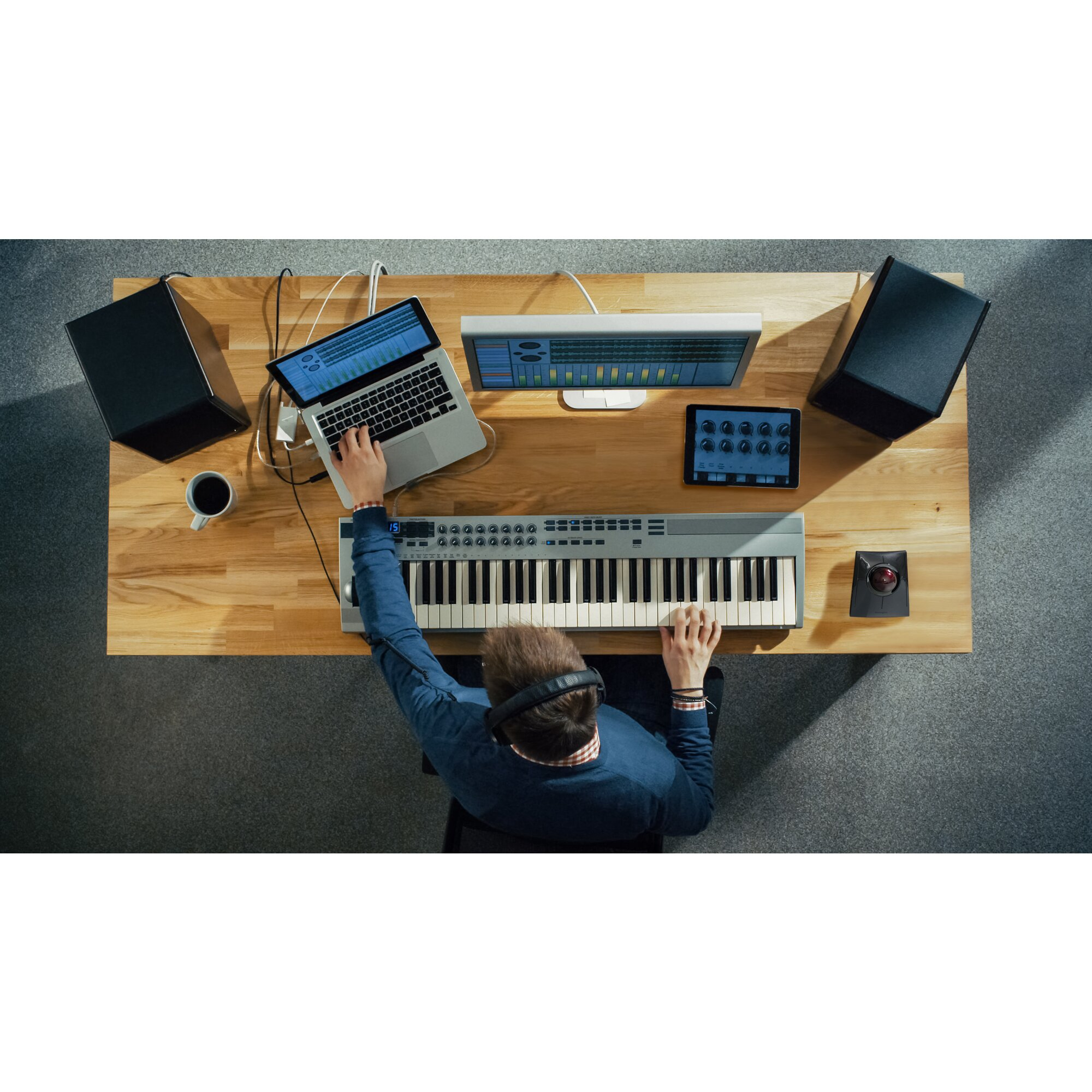 Mężczyzna gra na keyboardzie, laptop, monitor, tablet i głośniki na drewnianym biurku.