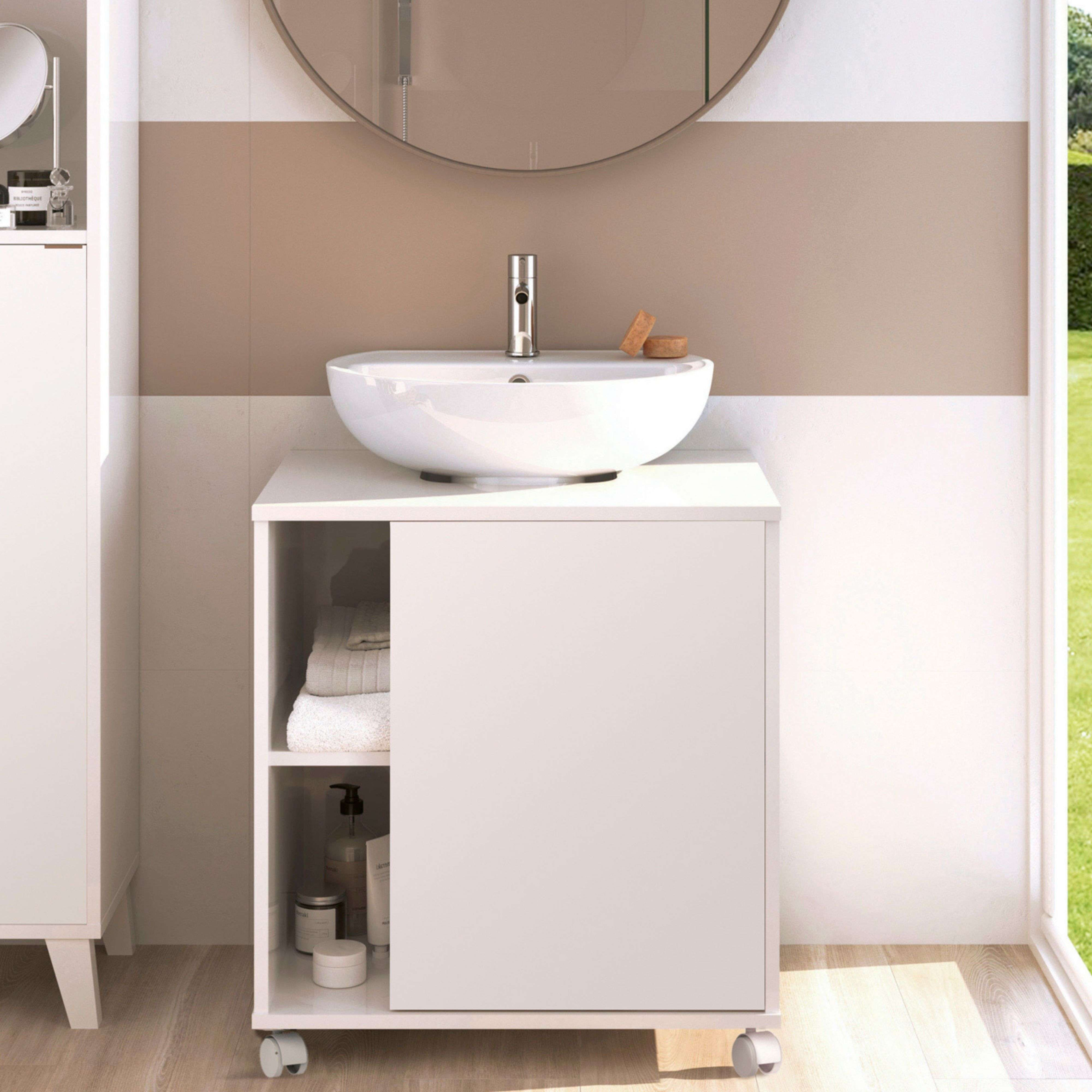 Un lavabo blanco se asienta sobre un mueble blanco con ruedas. Se ven toallas apiladas y lociones.