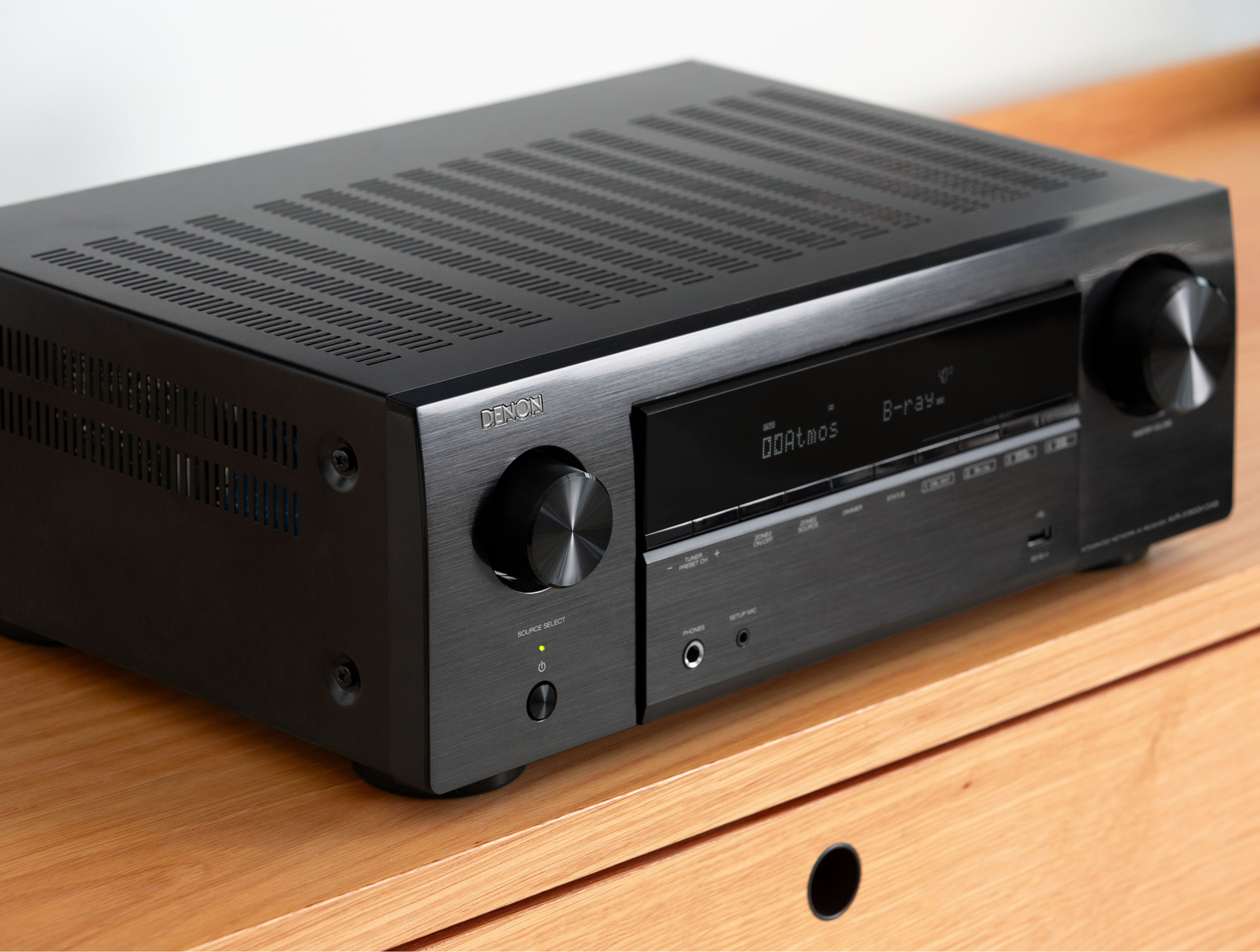 Schwarzer Denon AV-Receiver mit Display, Knöpfen und Lüftungsschlitzen auf einem Holztisch.