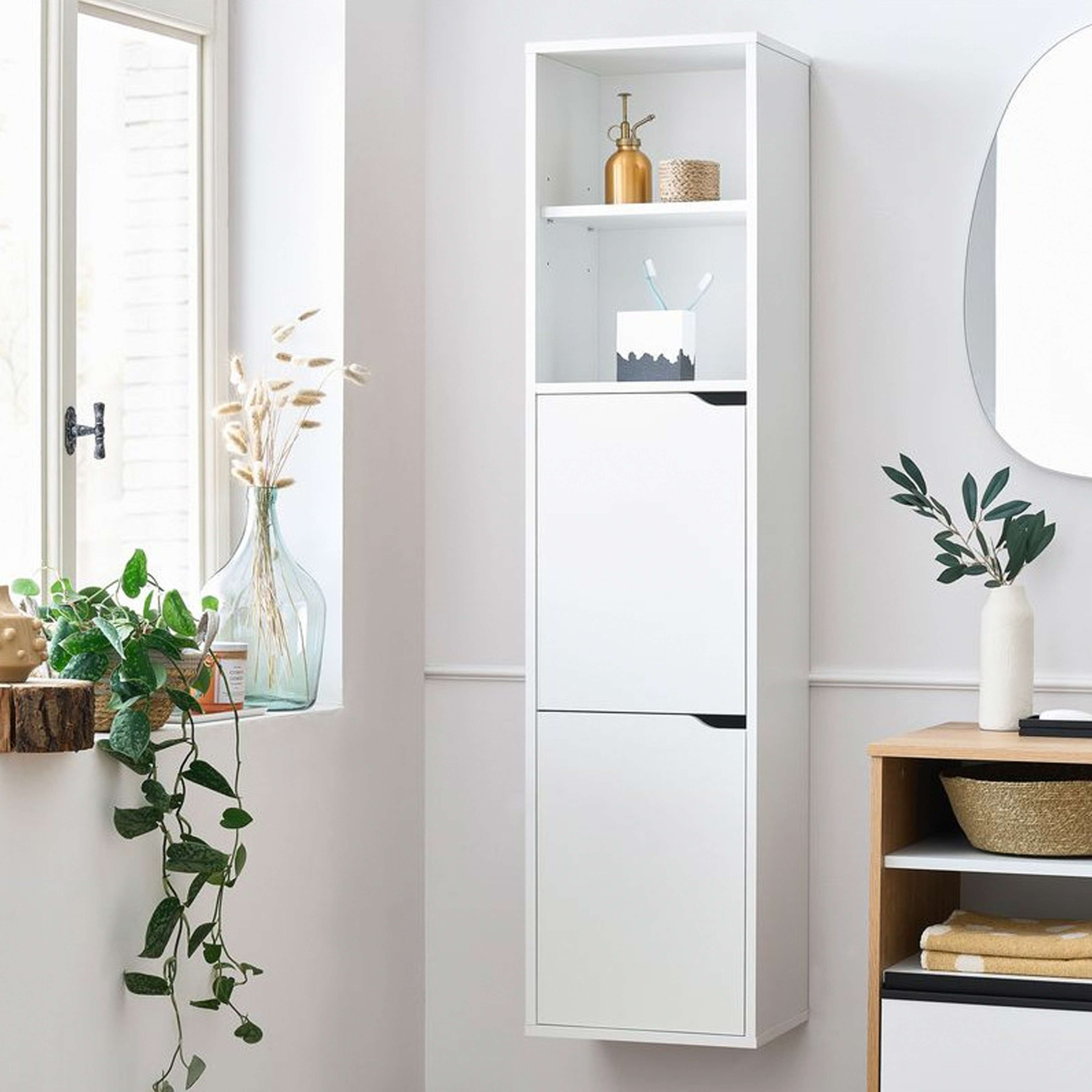 Un armario blanco, alto y estrecho, junto a una ventana con plantas.
