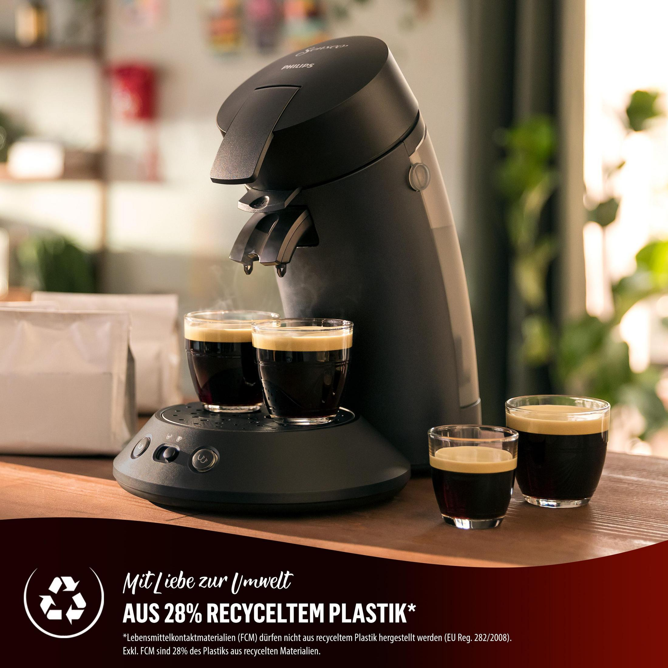 Eine schwarze Kaffeemaschine brüht drei Tassen Kaffee auf einem Holztisch.