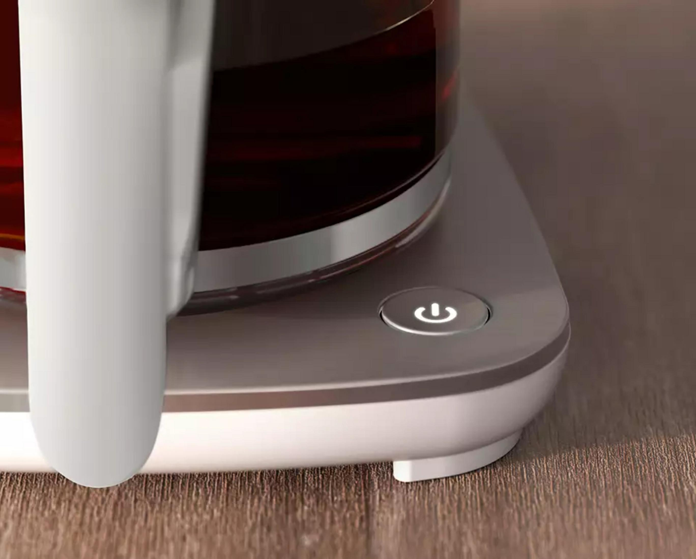 Biały uchwyt, szklany pojemnik z ciemnym płynem i świecący przycisk zasilania.