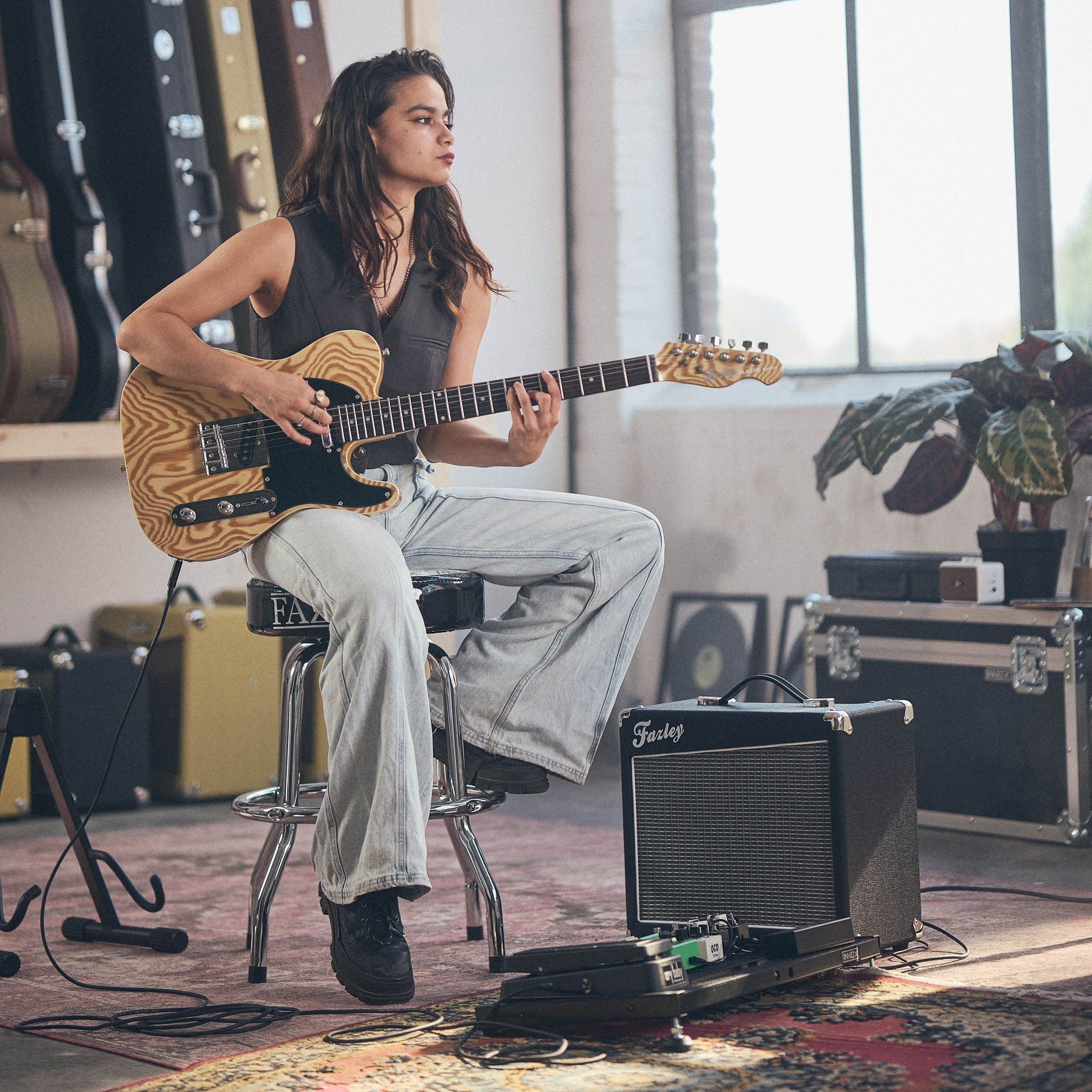 Een vrouw speelt gitaar in een kamer met gitaarkoffers en versterkers.