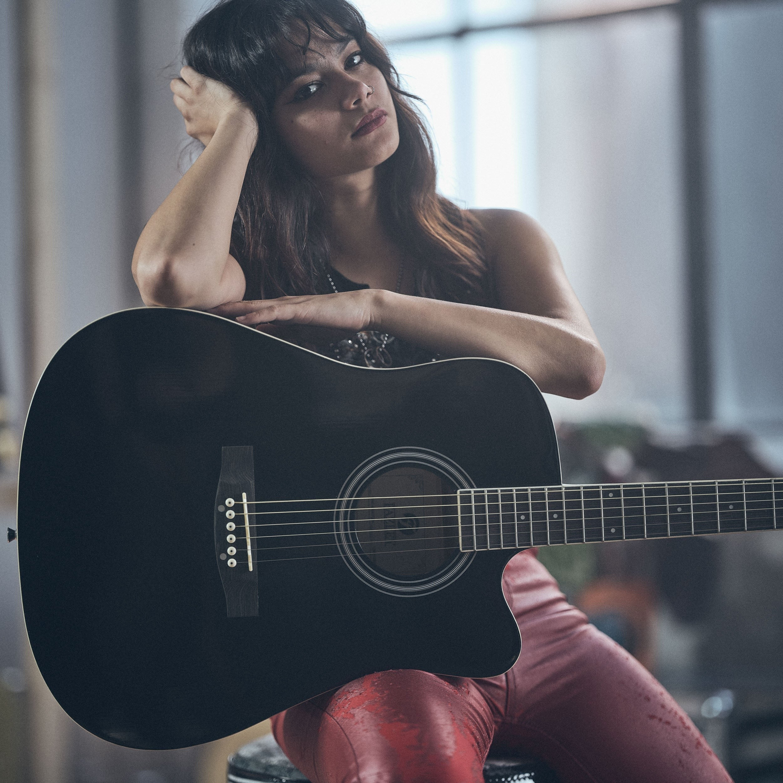 A woman with dark hair sits with a black guitar in front of her.