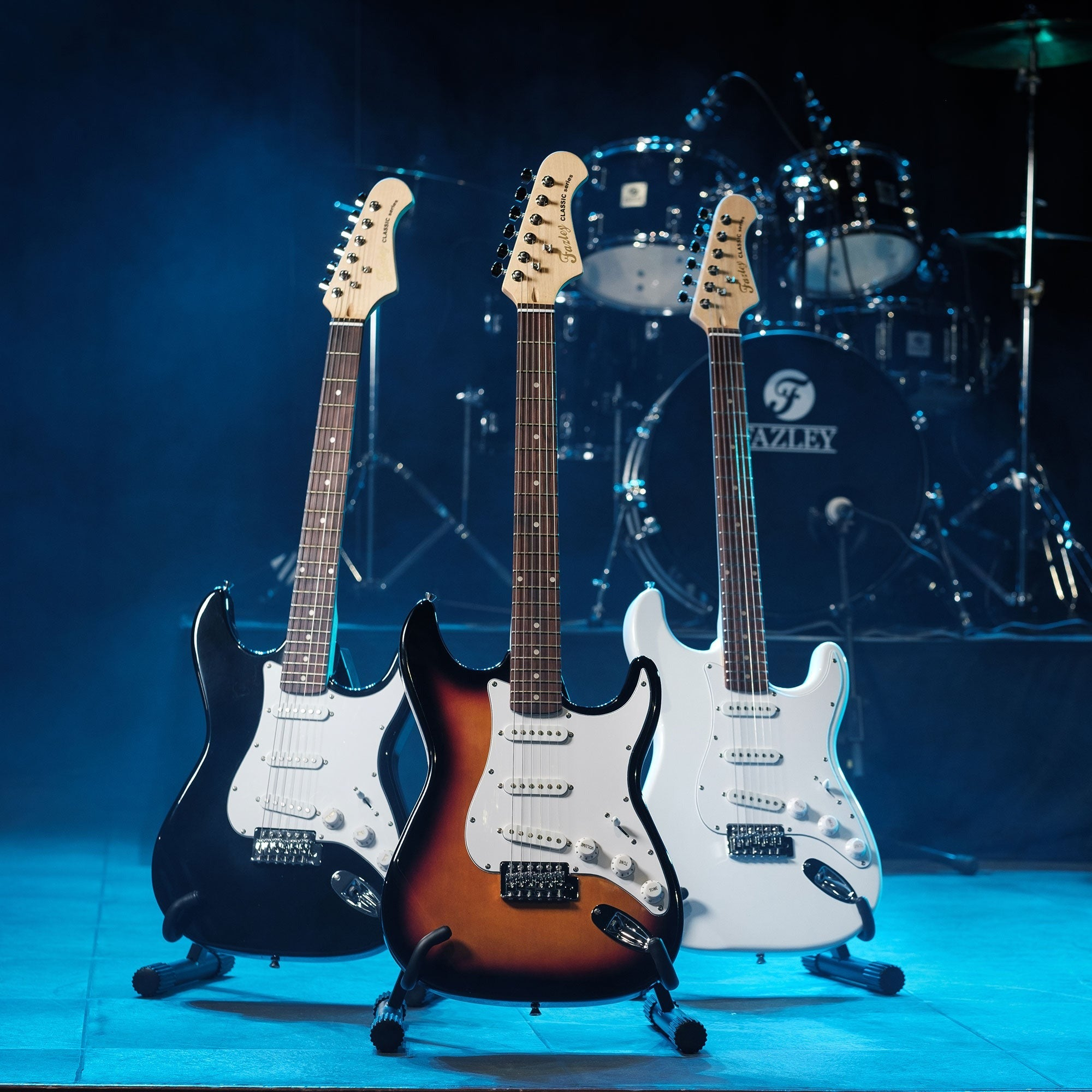 Drie elektrische gitaren voor een drumstel op een podium.