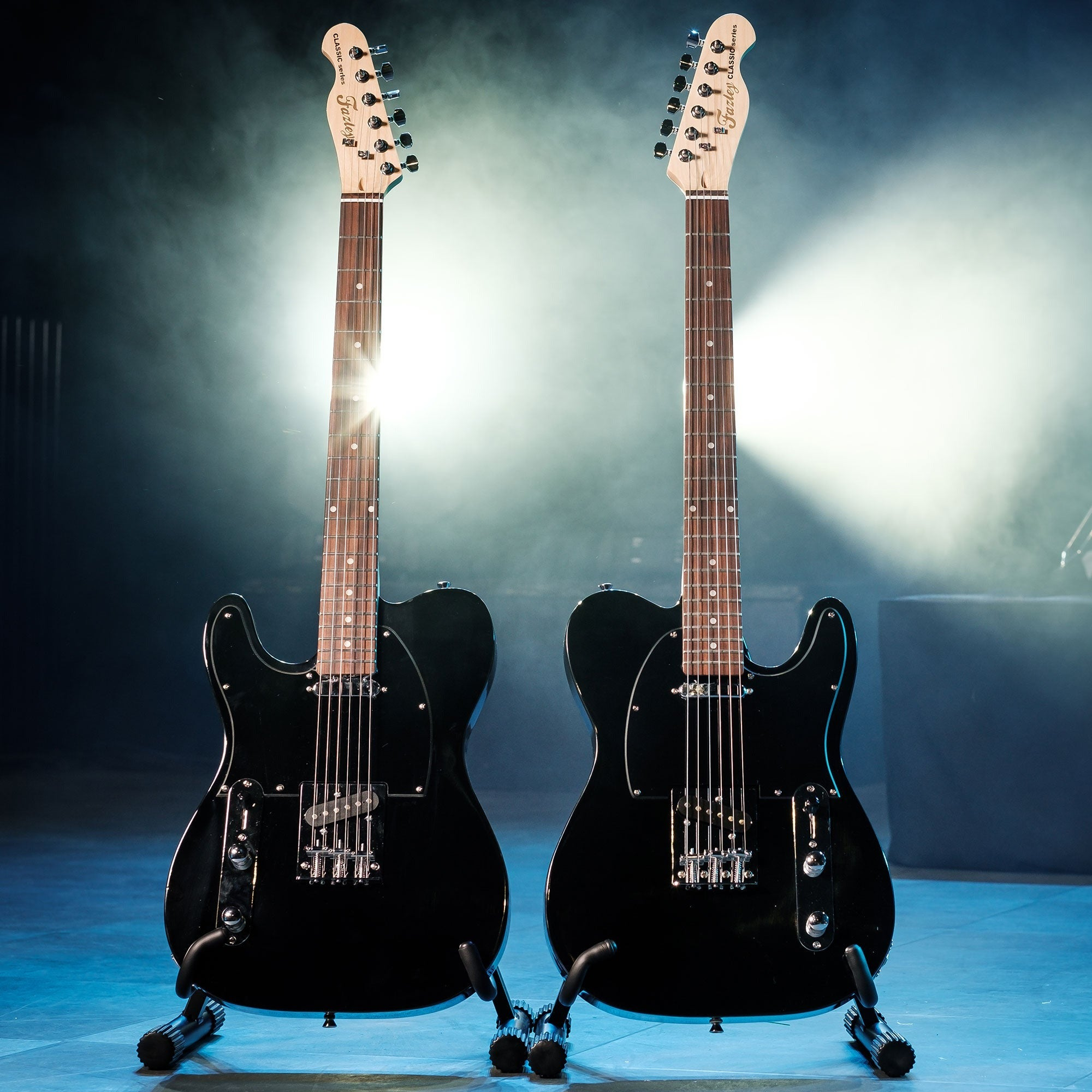 Twee zwarte elektrische gitaren op standaards in mist met spotlight.