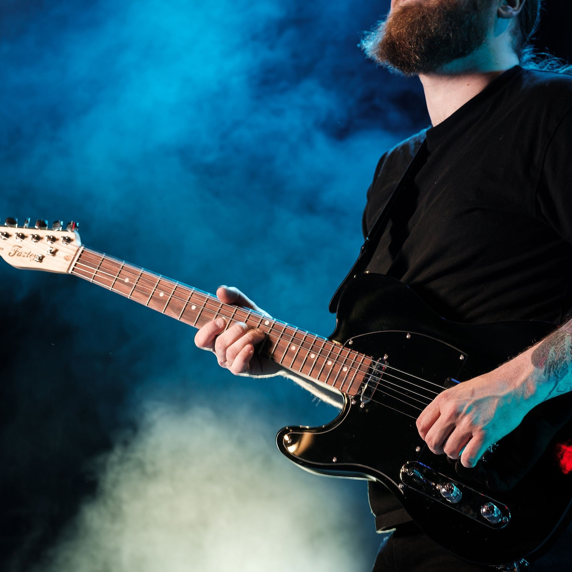 Een man bespeelt een zwarte elektrische gitaar met blauwe rook.
