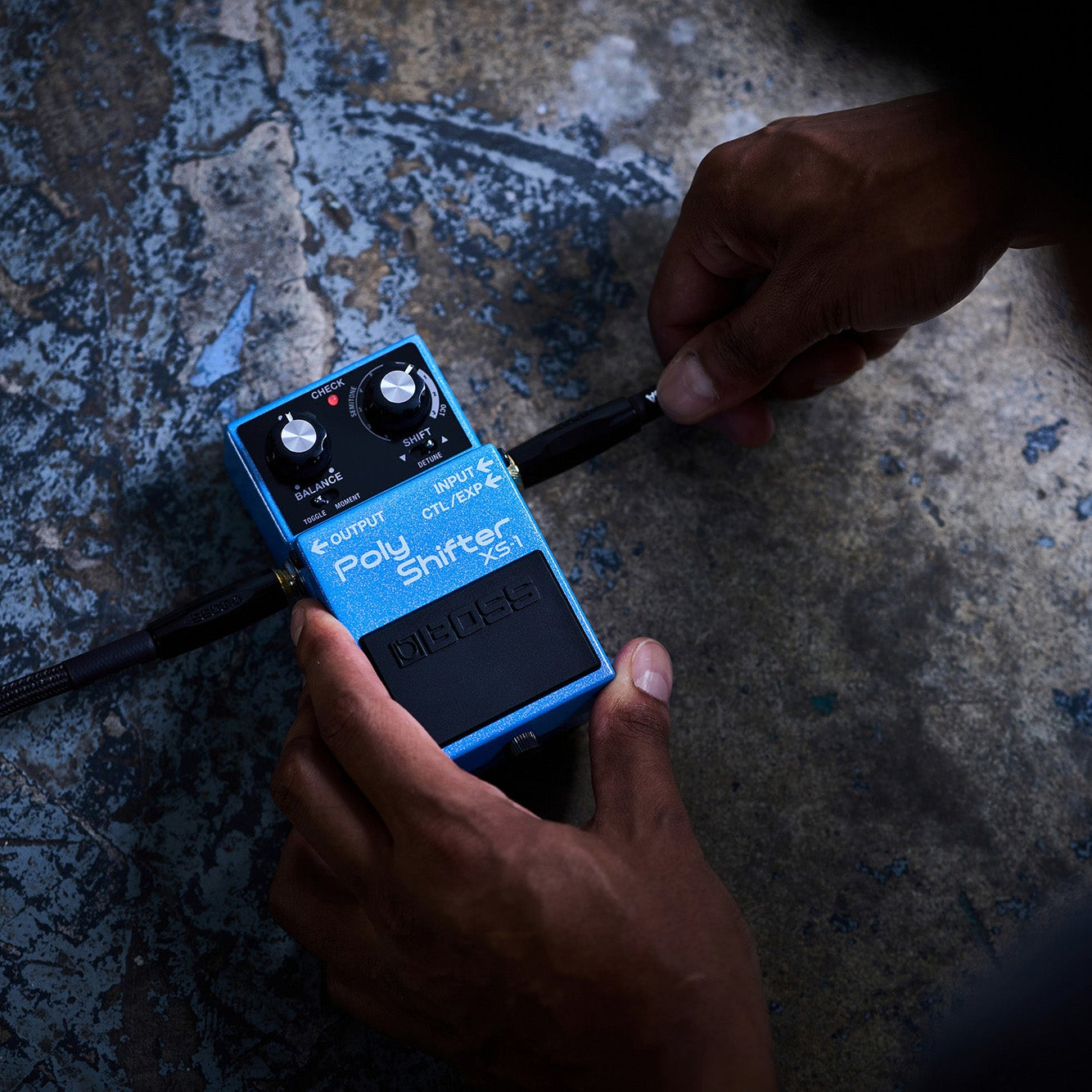 Blauw BOSS Poly Shifter XS-1 effectpedaal wordt in een kabel gestoken.