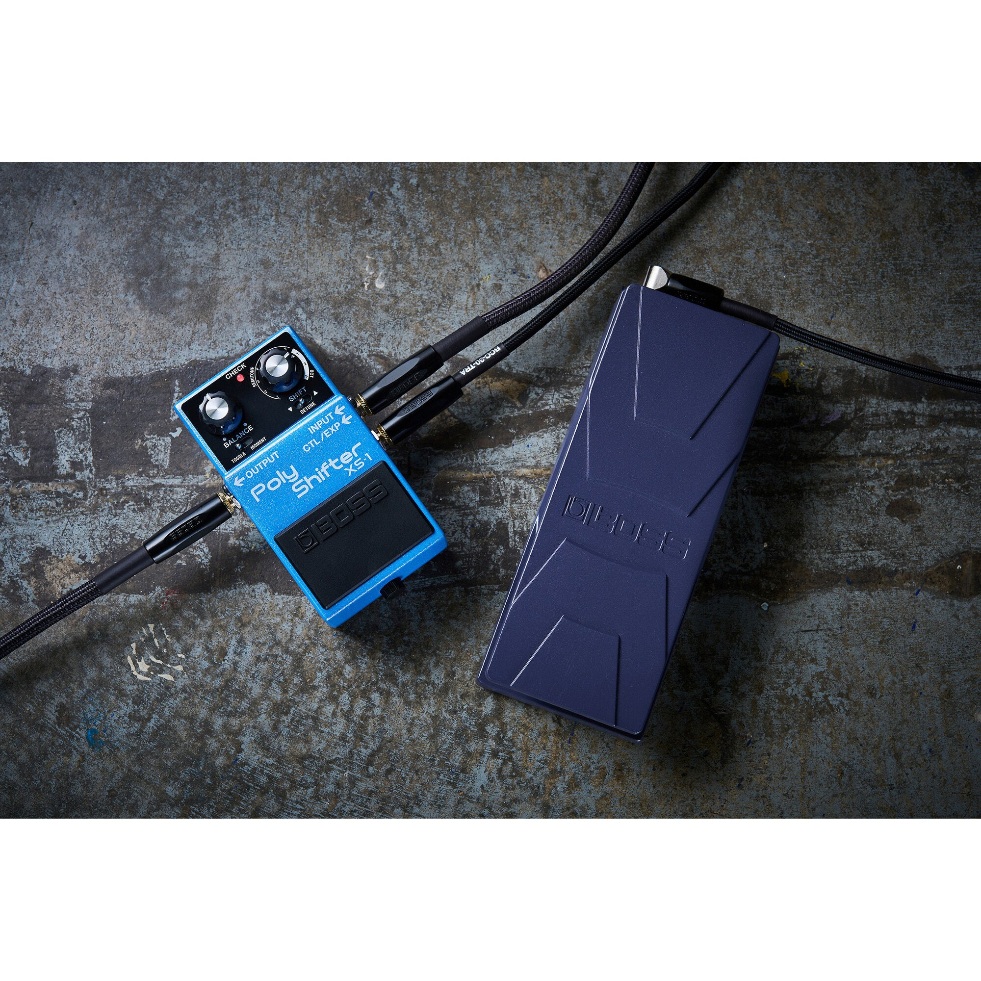 Blauwe BOSS Poly Shifter XS-1 gitaareffectpedaal met zwarte kabels op ruw oppervlak.
