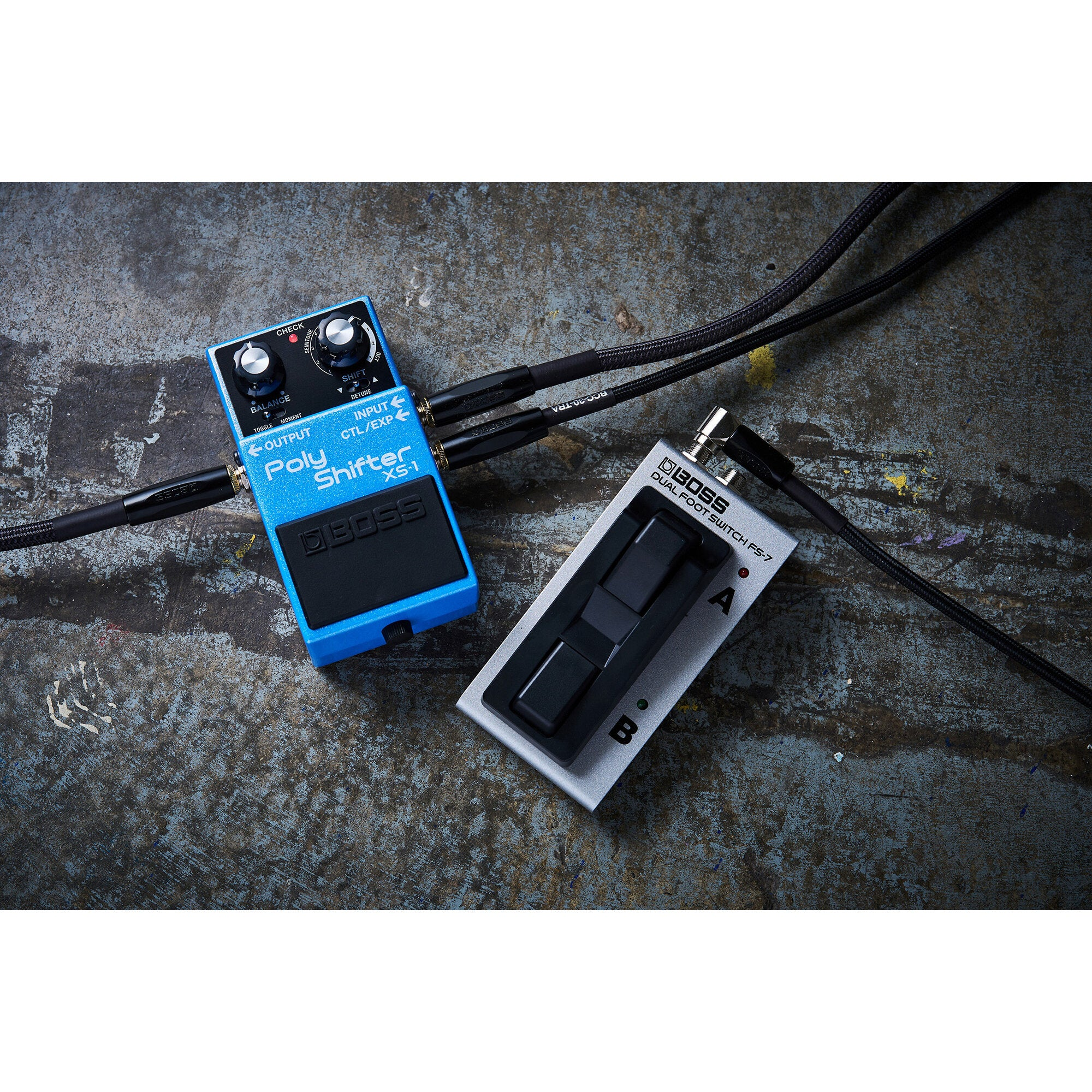 Een blauwe BOSS Poly Shifter XS-1 en een zilveren BOSS FS-7 voetschakelaar met kabels op beton.