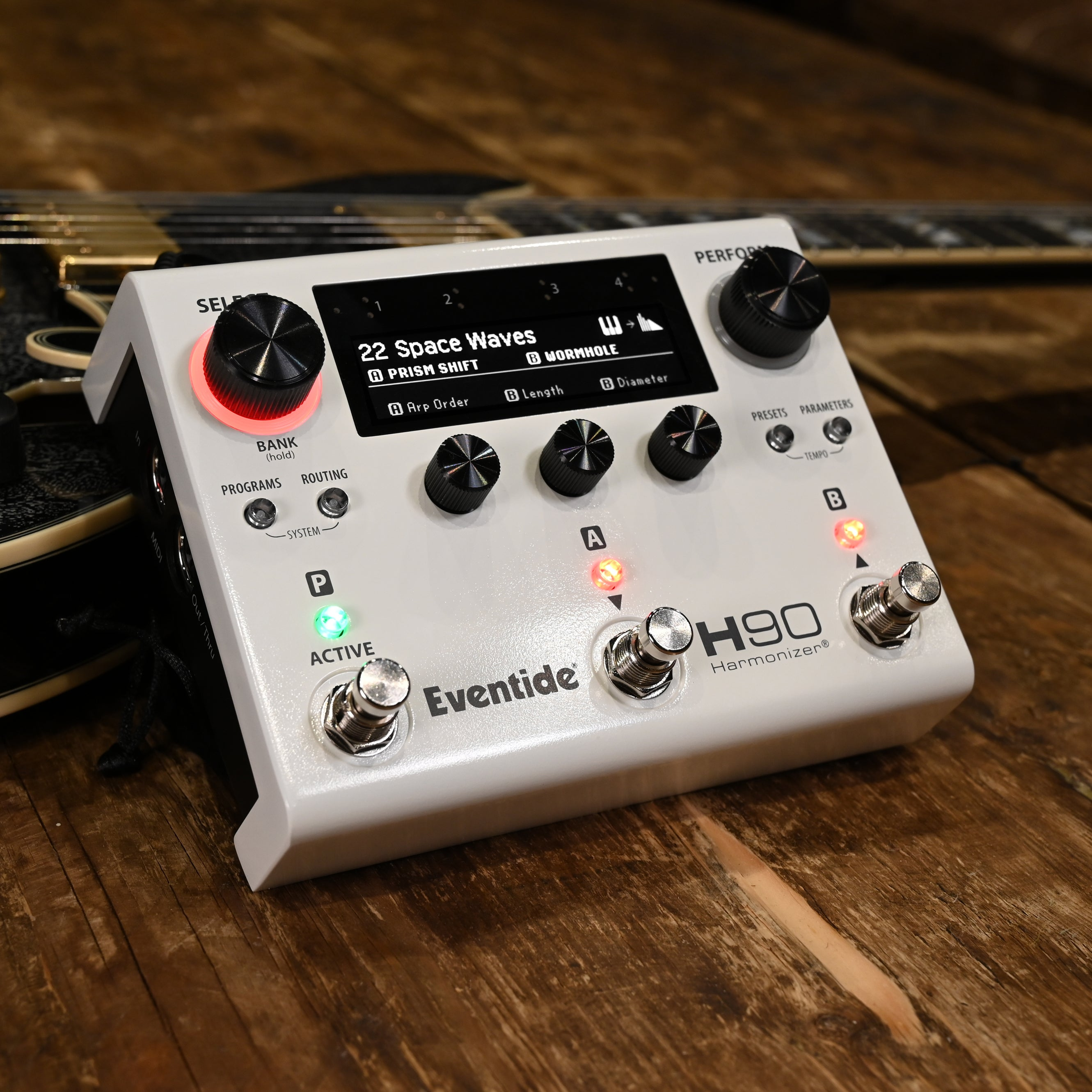 Een wit Eventide H90 Harmonizer pedaal op een houten tafel naast een gitaar.
