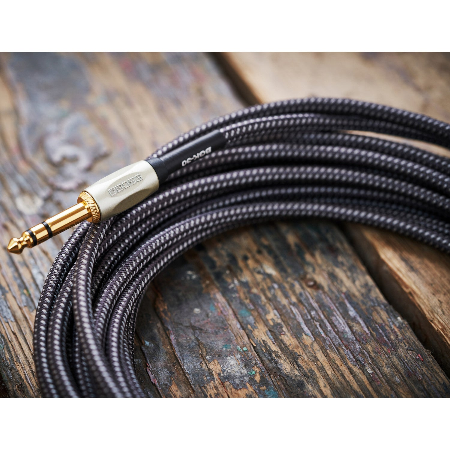 Een zwart gevlochten kabel met gouden connector ligt op hout.