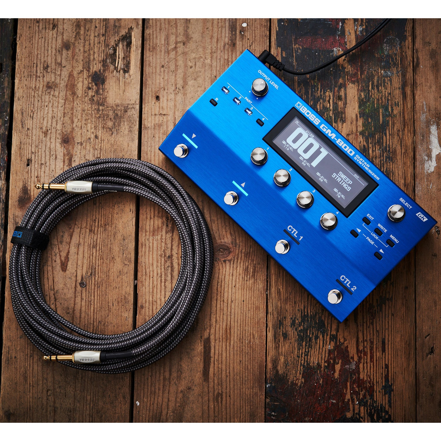 Een blauwe BOSS GM-800 gitaarsynthesizer met kabel op houten vloer.