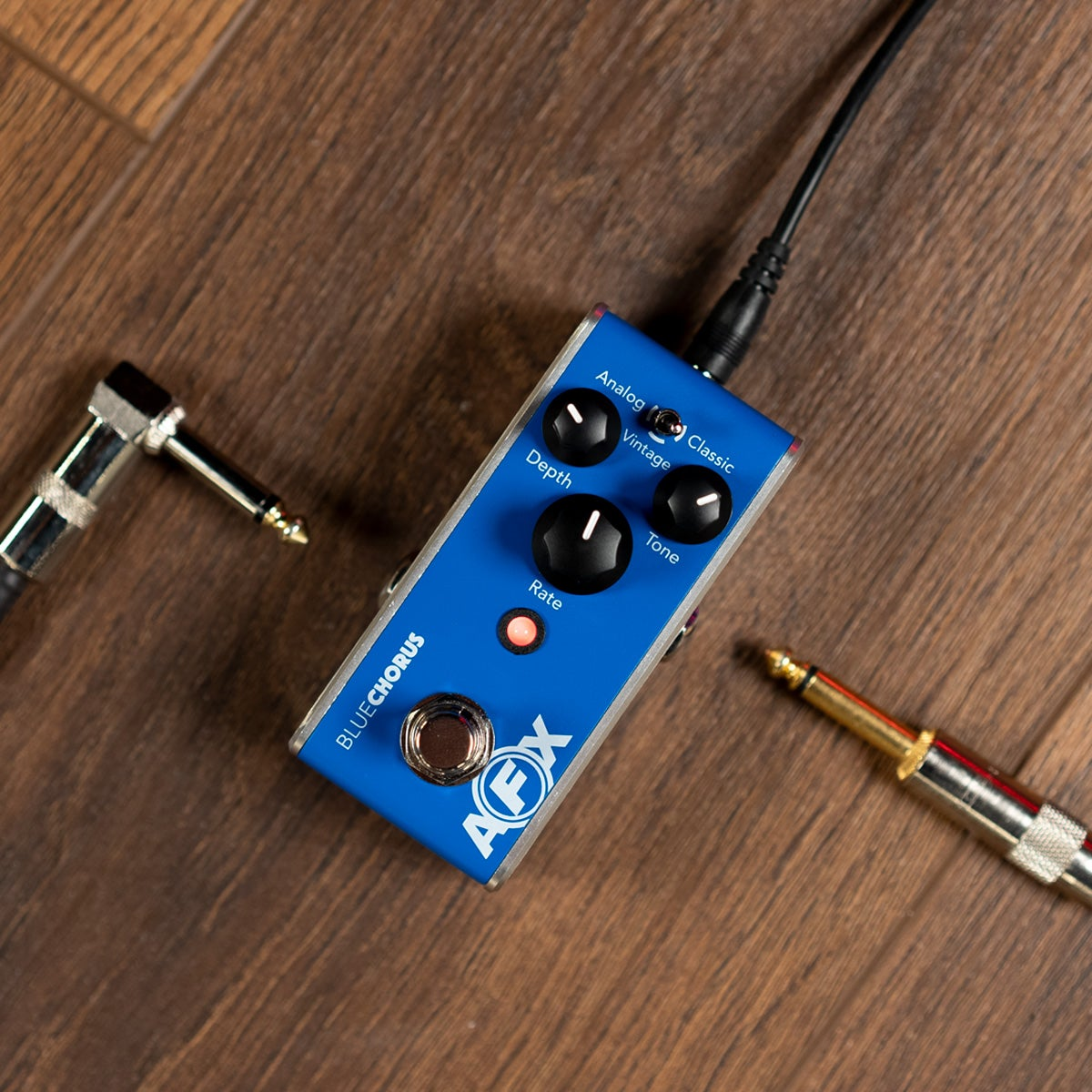 Blue analog chorus guitar pedal with knobs and cables on wood.