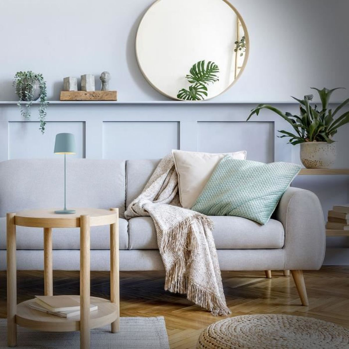 Ein hellgraues Sofa mit Kissen und Decke, daneben ein Holztisch mit Lampe.