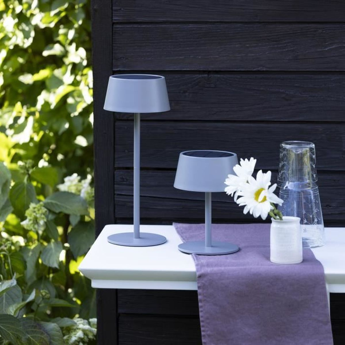 Zwei graue Lampen und eine Blume auf einem Tisch vor einem Holzhaus.