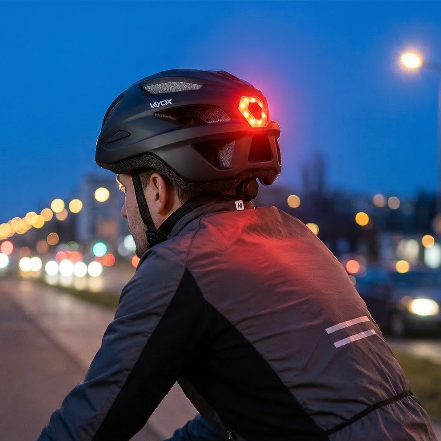 Kolarz w kasku i z czerwonym światłem tylnym w nocy, ruch miejski.