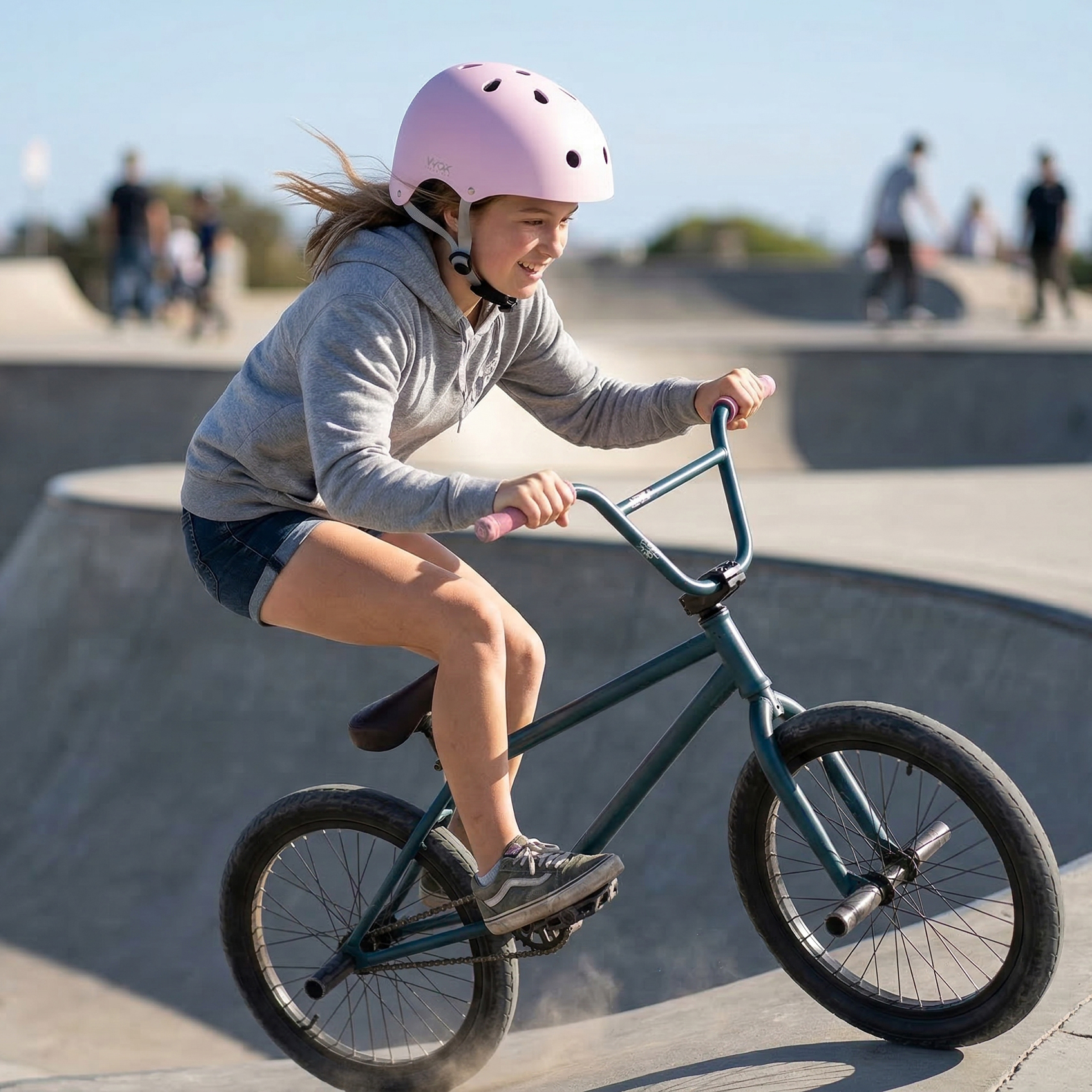 Dziewczynka w różowym kasku jeździ na BMX-ie w skateparku.