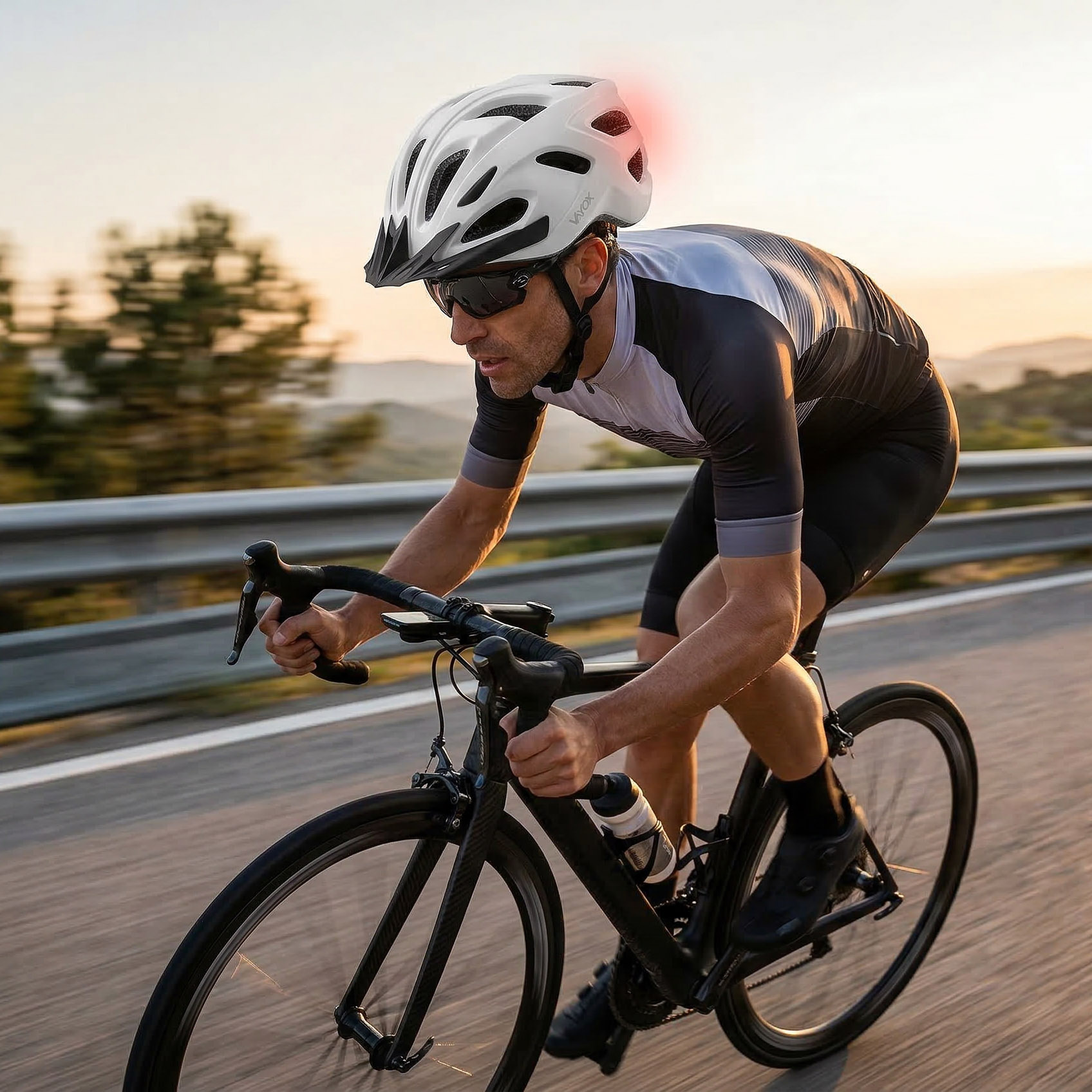 Mężczyzna jedzie na rowerze szosowym w białym kasku z czerwonym światłem pozycyjnym o zachodzie słońca.