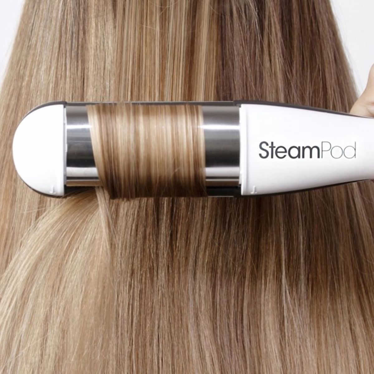 Ein Dampfglätteisen glättet blondes Haar mit Strähnchen.