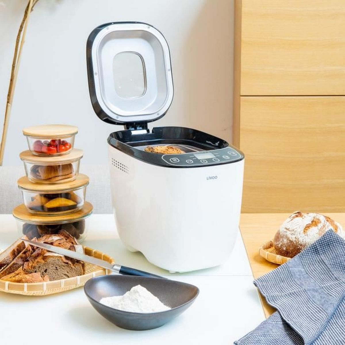 Brotbackautomat mit Brot, Schalen und Zutaten auf einem Tisch.