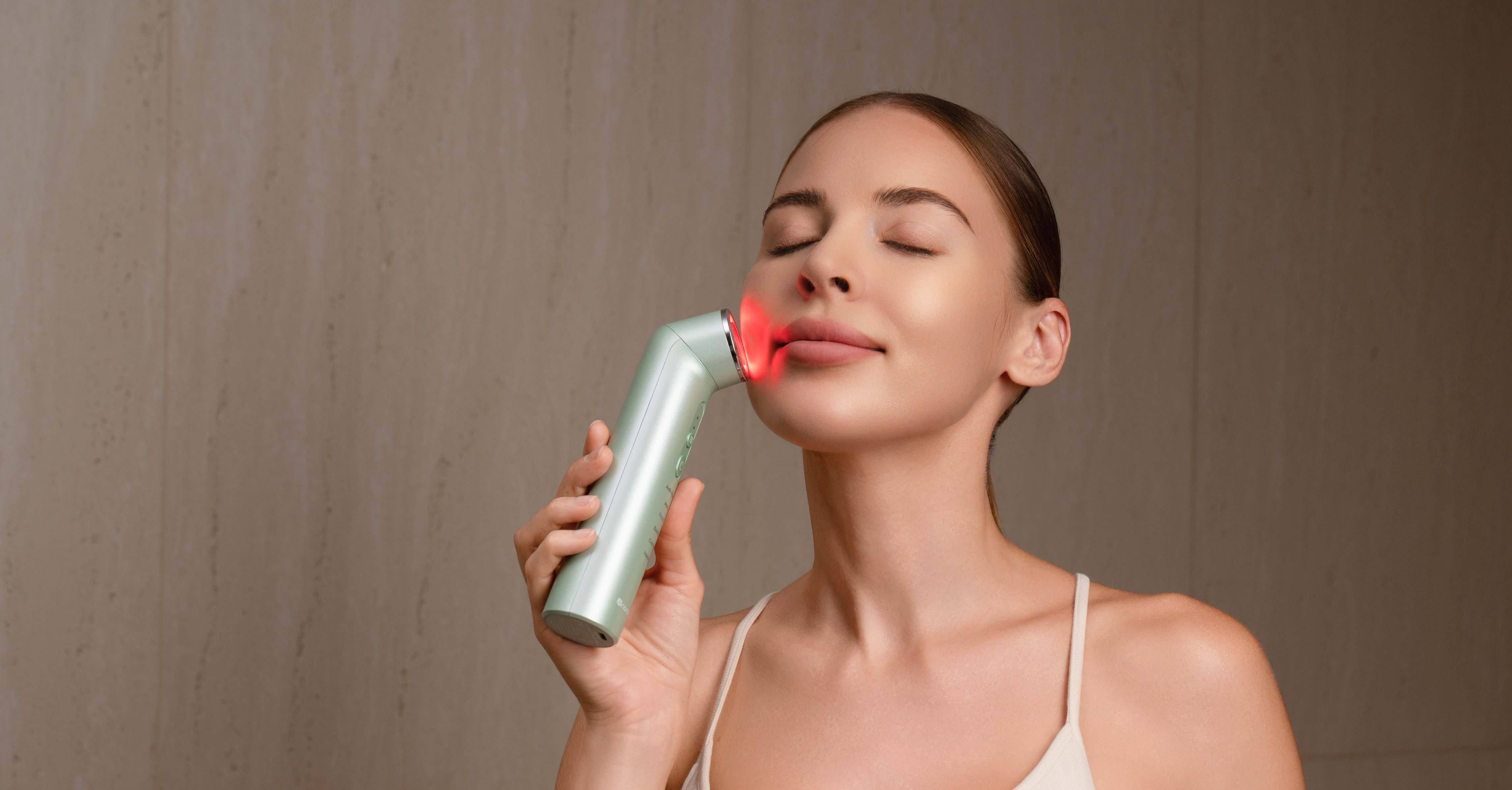 Una donna usa un dispositivo di bellezza verde con luce rossa sul viso.