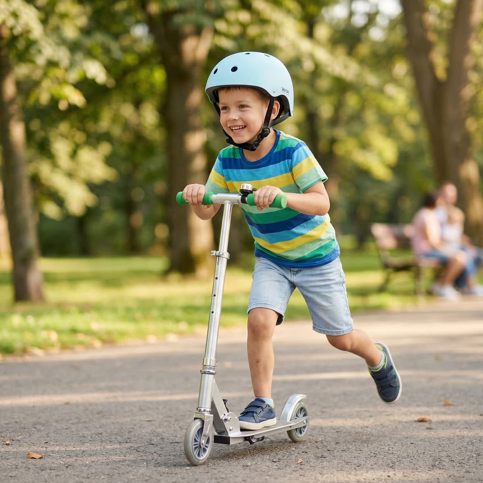 Chłopiec jedzie na hulajnodze w parku, ma na głowie kask i koszulkę w paski.