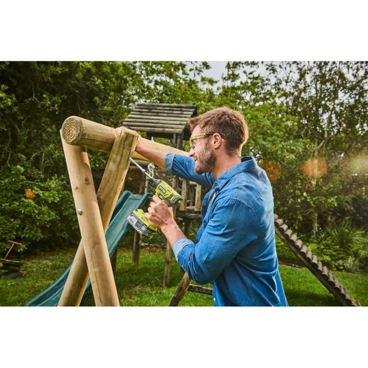 Mann mit Bohrmaschine baut Holzschaukel im Garten.