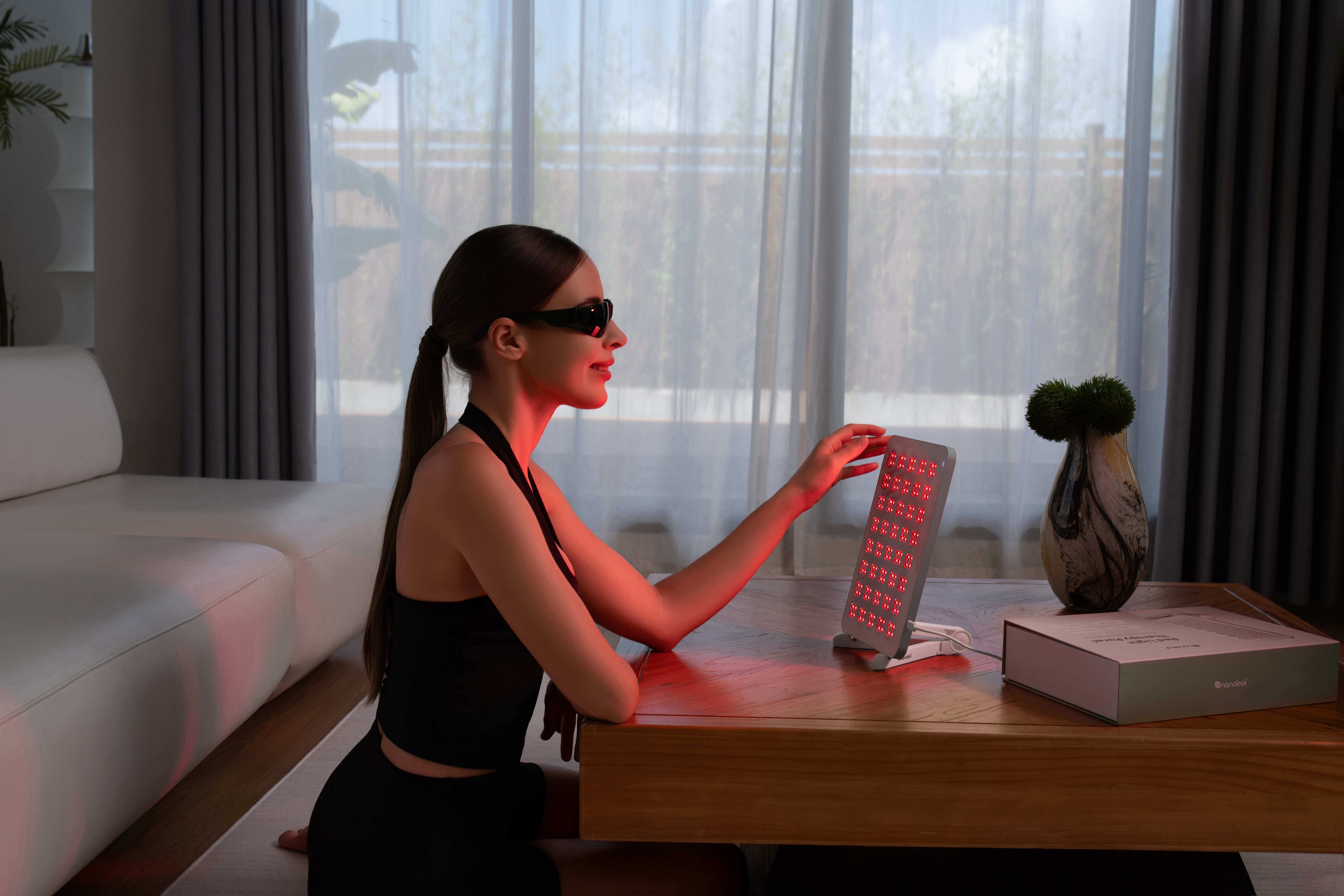 Eine Frau mit Schutzbrille sitzt vor einer roten Lichttherapieplatte.
