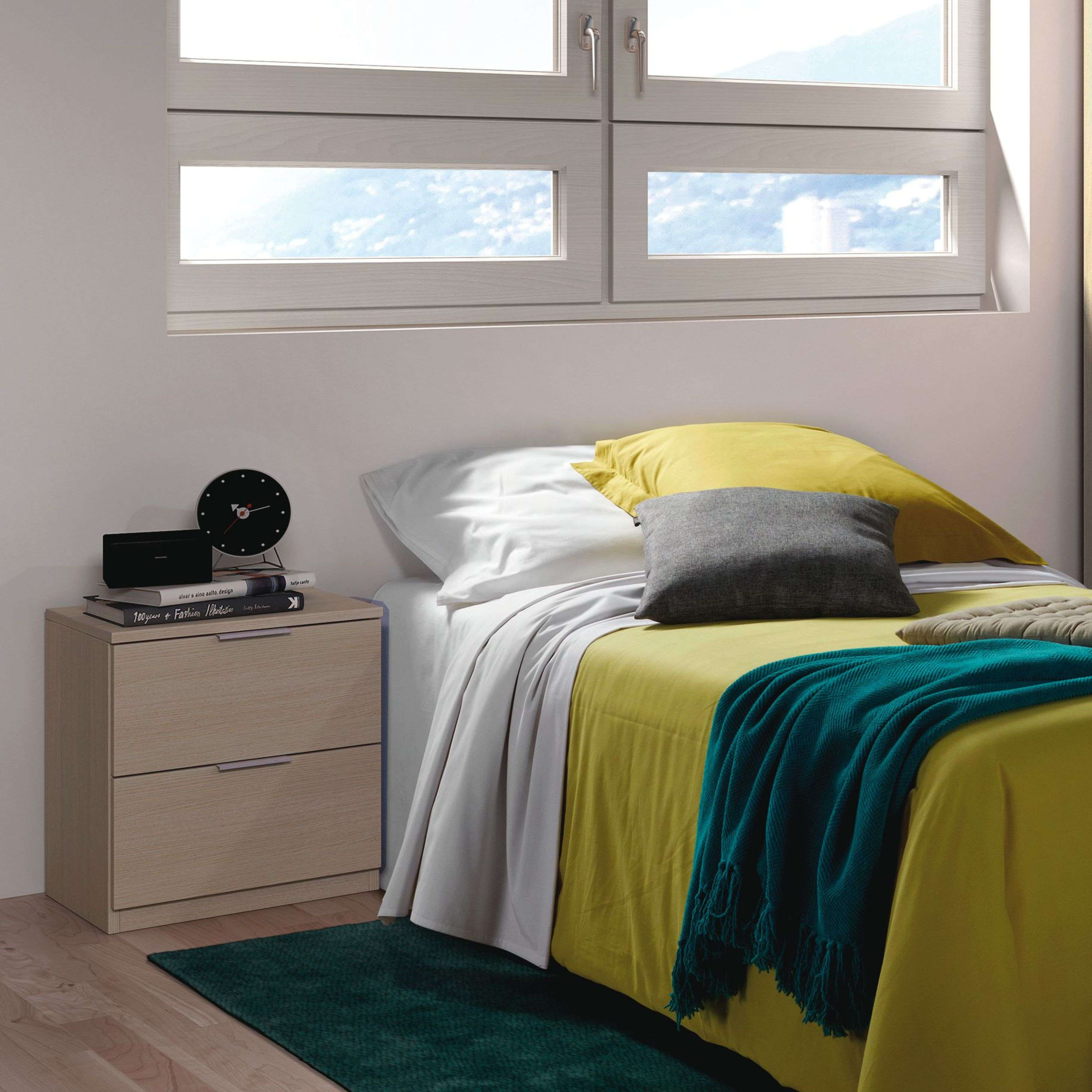 Un dormitorio con edredón amarillo, manta turquesa y mesita de noche con libros.