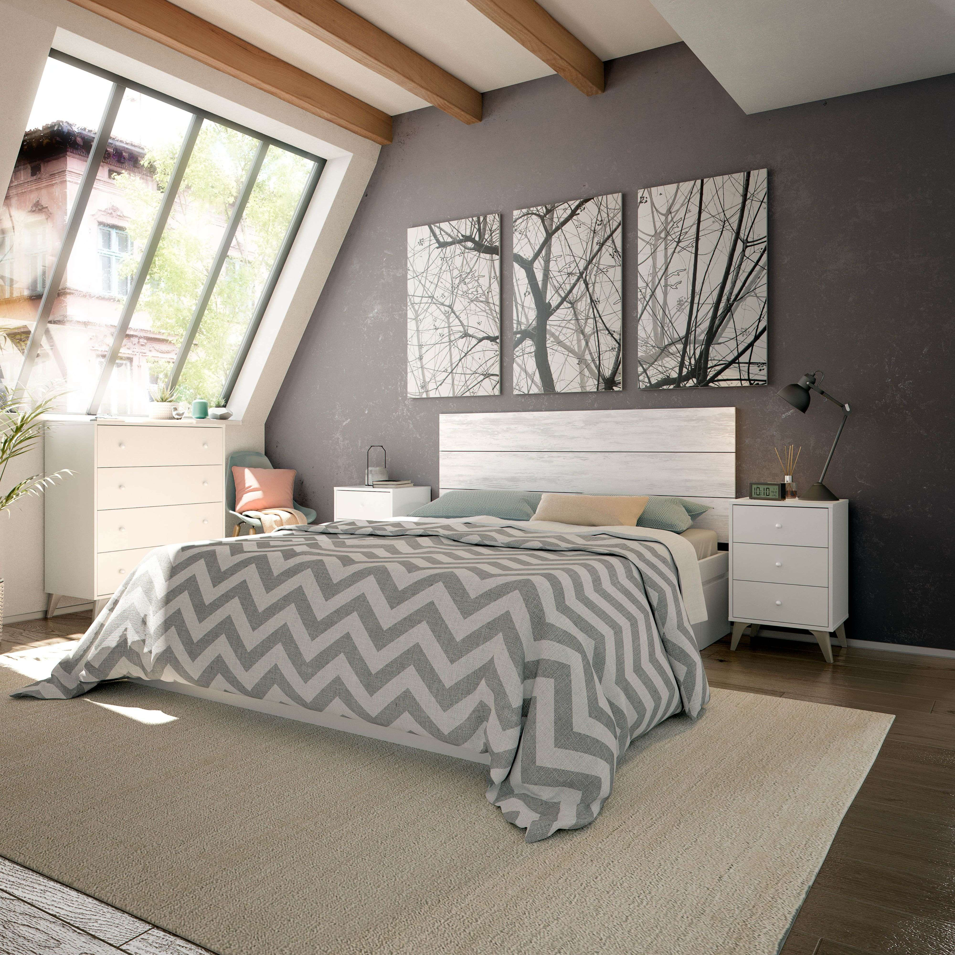 Un dormitorio con ventana inclinada, cama con manta gris y blanca, mesitas de noche y arte de pared.