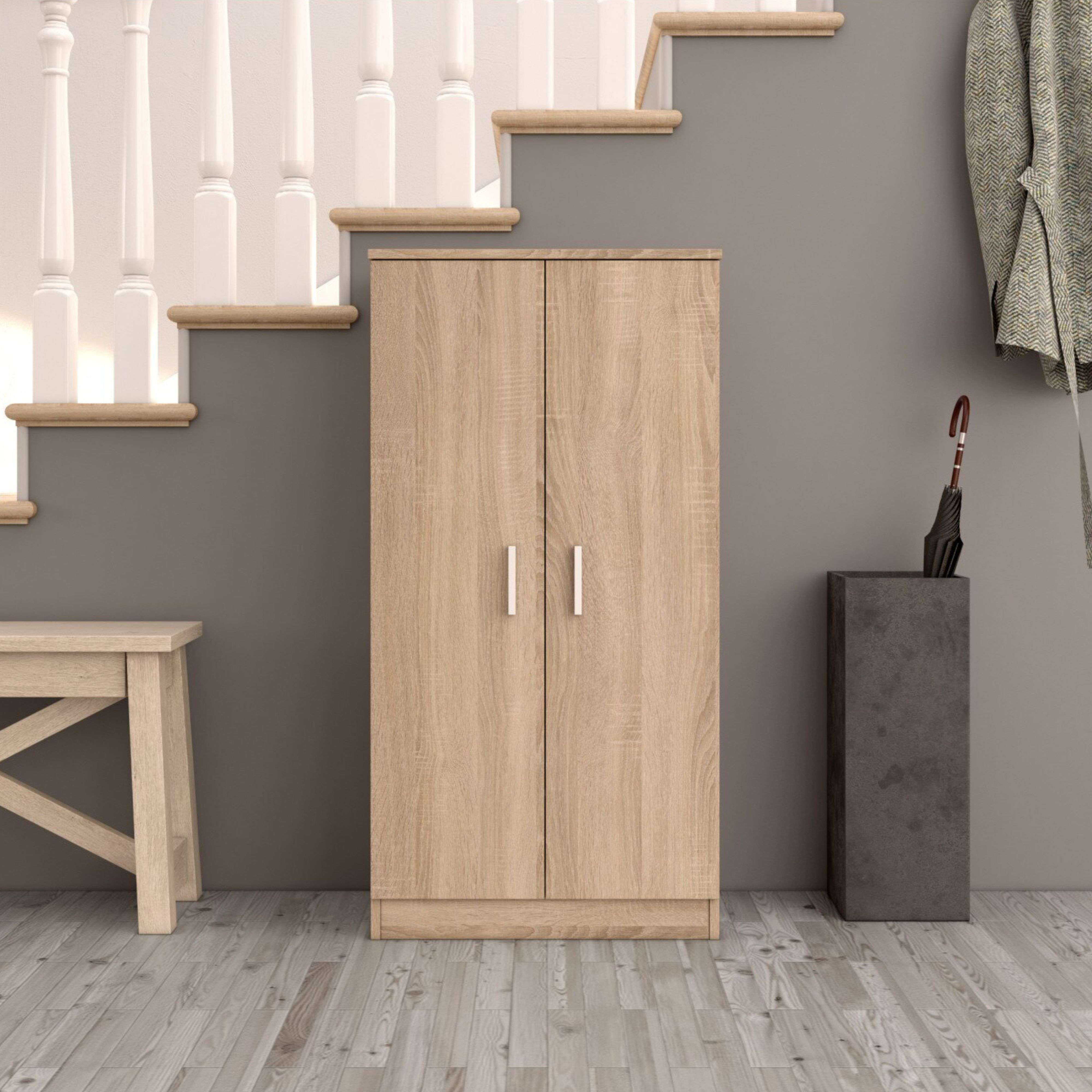 Un armario de madera clara junto a una escalera con balaustres blancos. También se ven un taburete y un paragüero.