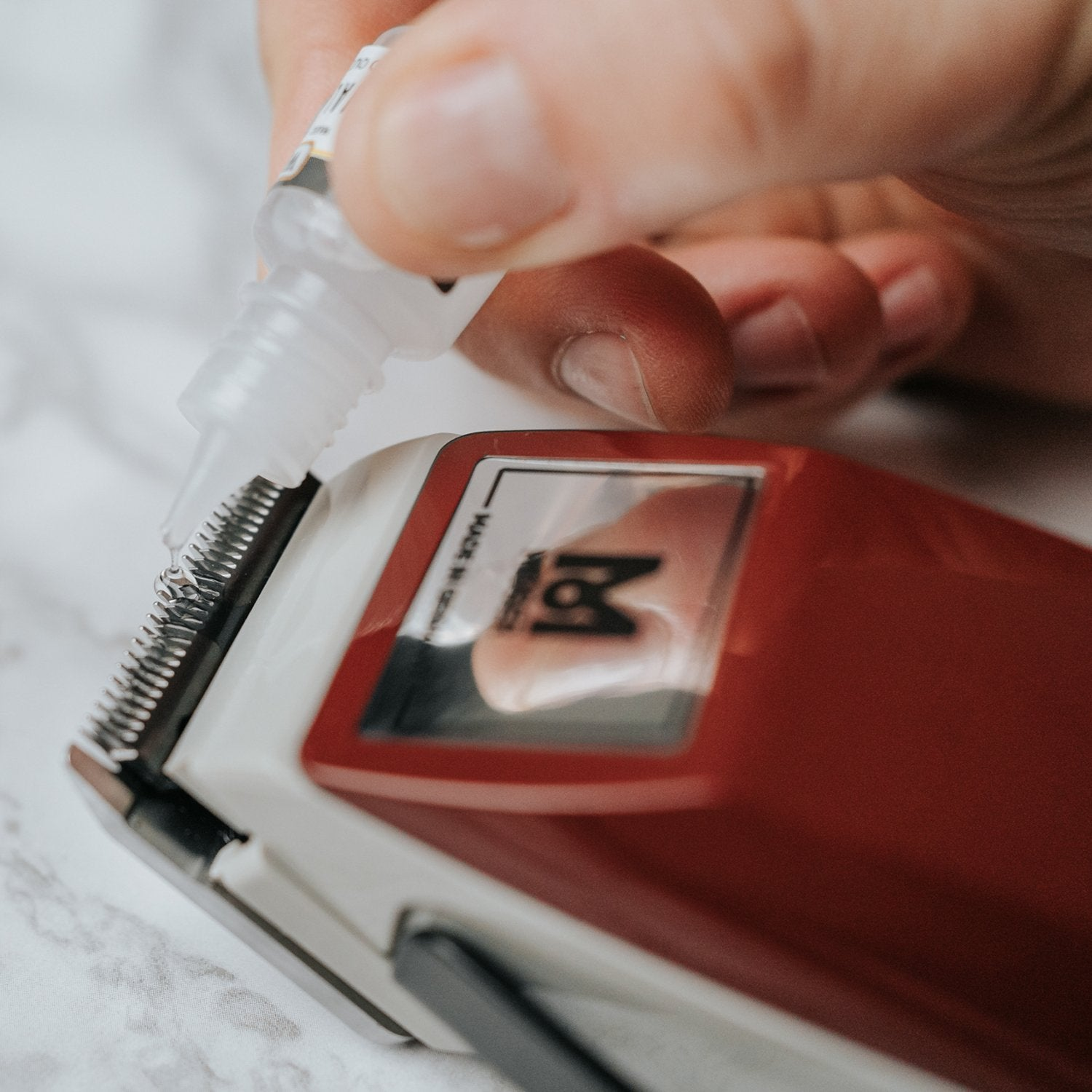 A hand drips oil onto a red and white hair clipper.