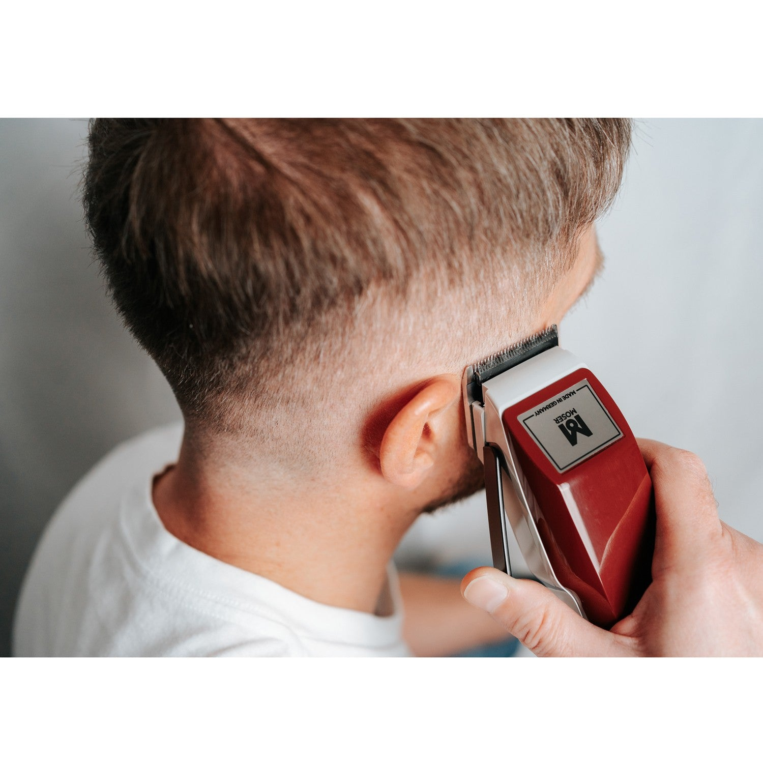 A red hair clipper is being used on a man's head.