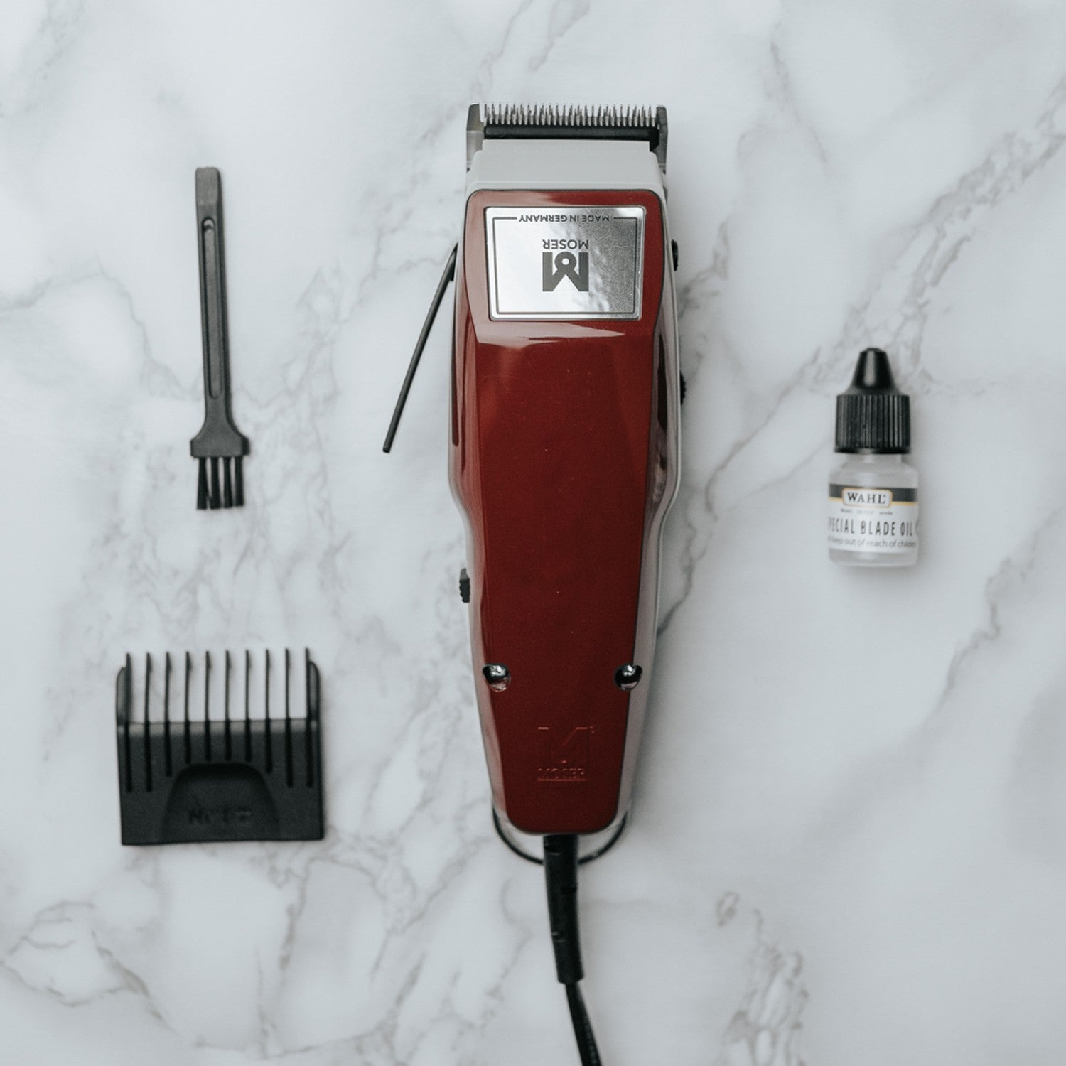 A red hair clipper with accessories on a marble surface.
