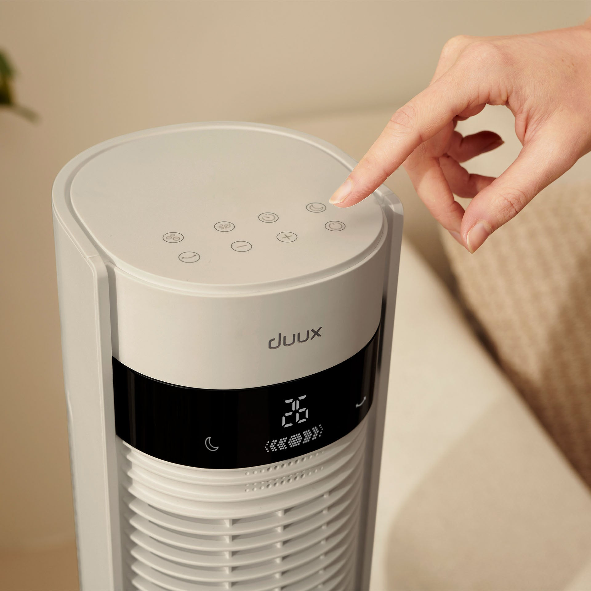 Een hand drukt op een knop van een witte torenventilator met digitaal display.