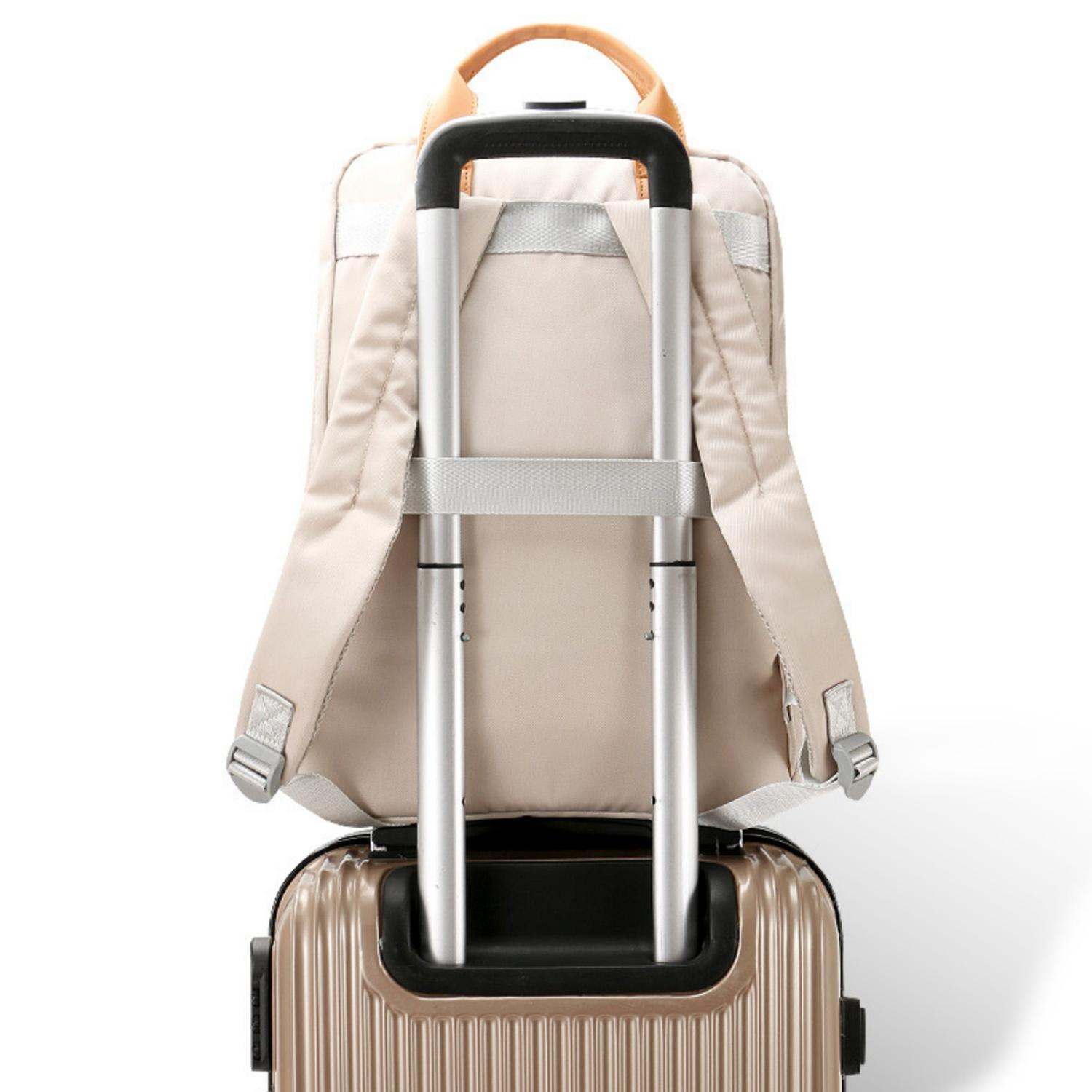 Ein beiger Rucksack sitzt auf einem bronzefarbenen Rollkoffer mit silbernem Griff.
