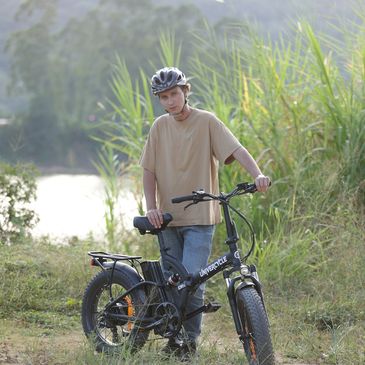 Mężczyzna w kasku stoi obok czarnego roweru elektrycznego na zewnątrz, otoczony zielenią.