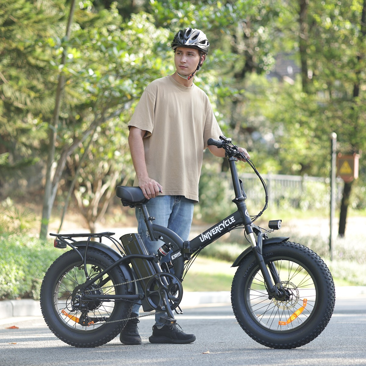 Mężczyzna w beżowej koszulce i kasku stoi obok czarnego roweru składanego.