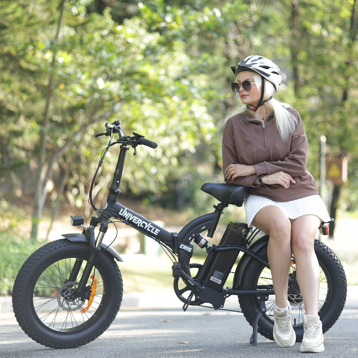 Kobieta w kasku siedzi na czarnym rowerze elektrycznym na zewnątrz na ścieżce.
