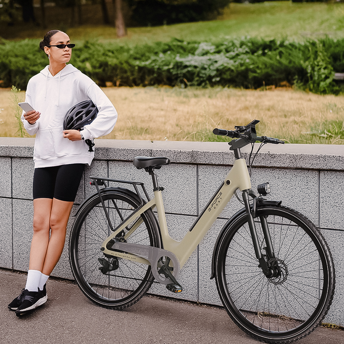 Kobieta z kaskiem i telefonem opiera się o rower przy murze.