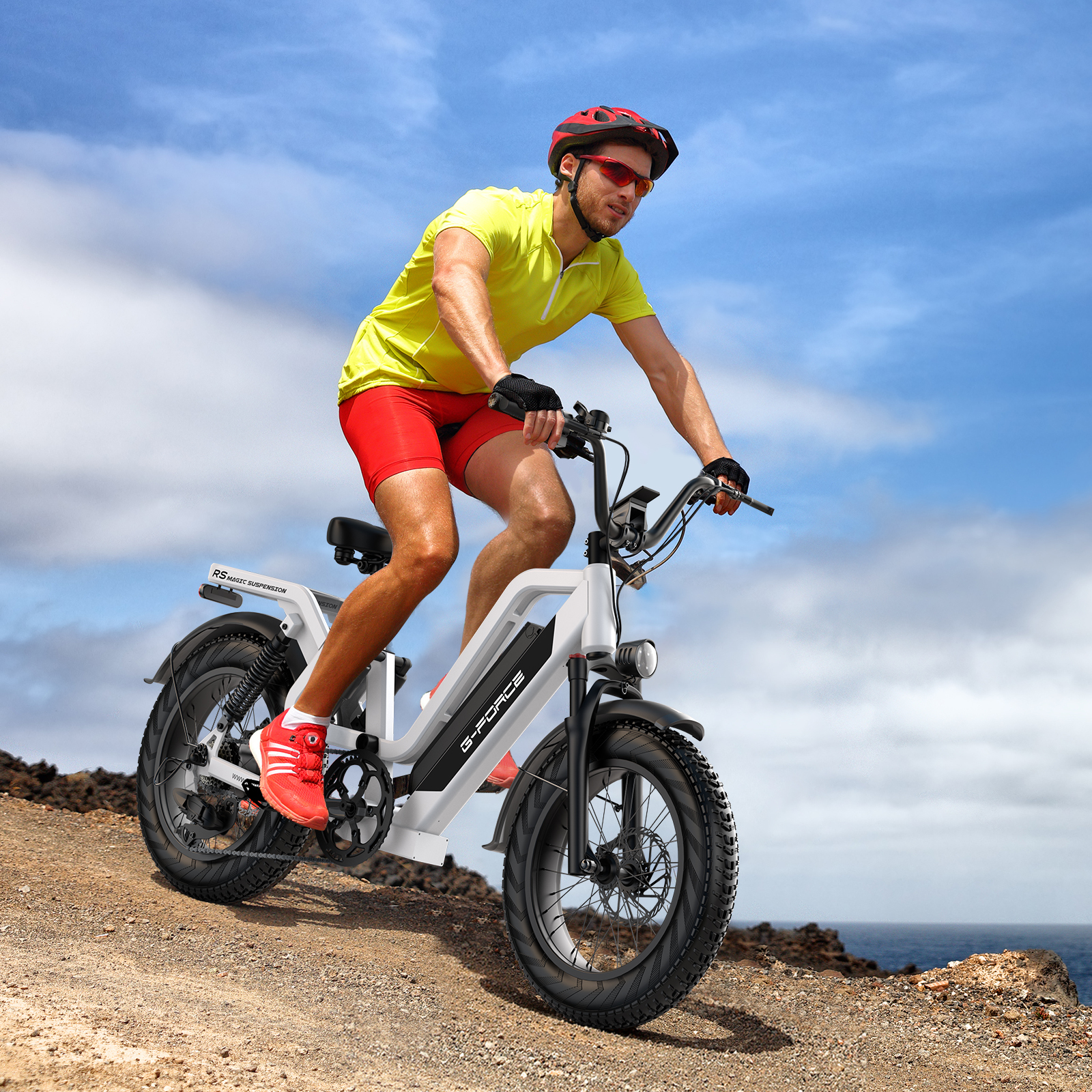 Mężczyzna w żółtej koszulce i czerwonych spodenkach jedzie białym rowerem elektrycznym po skalistej ścieżce przybrzeżnej.