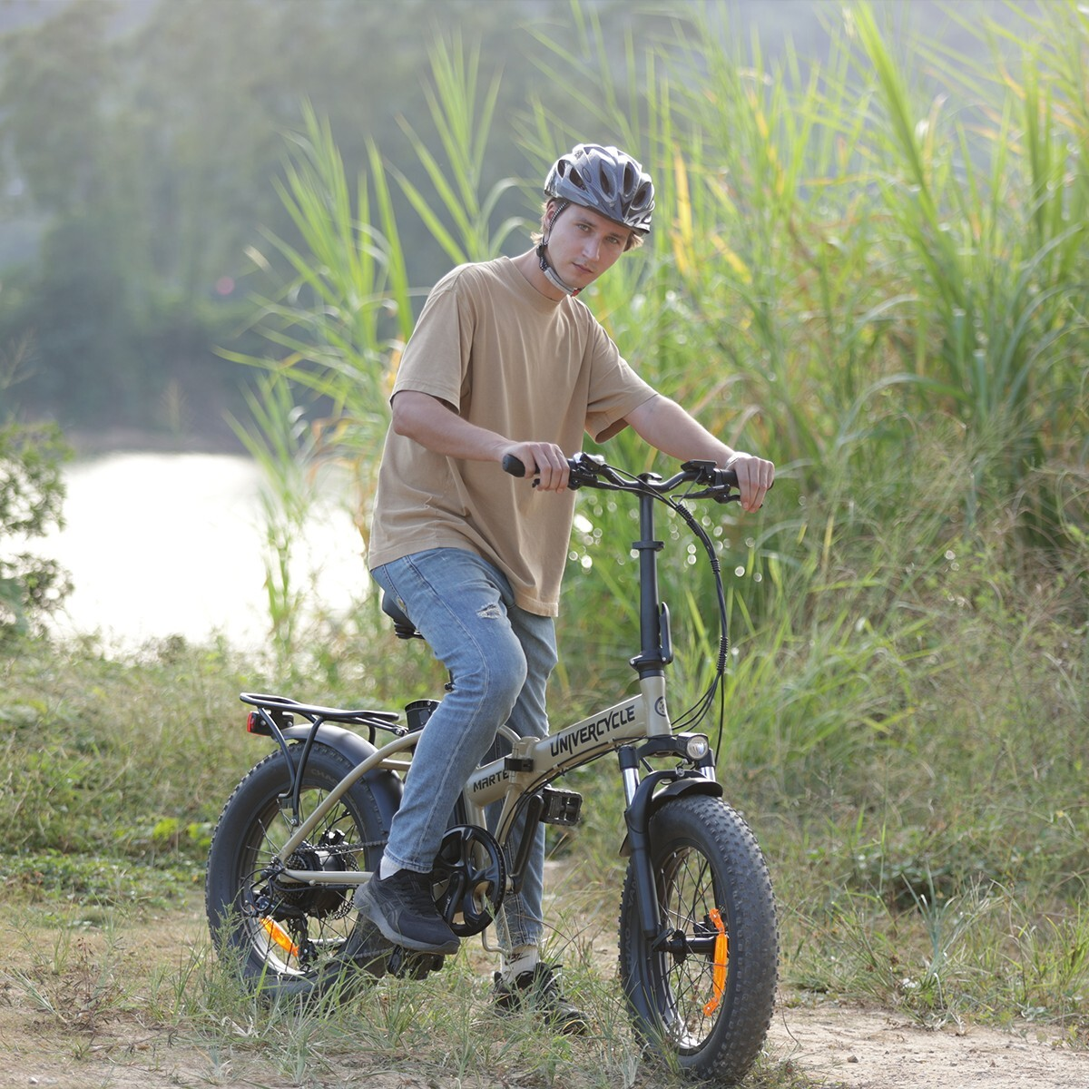 Mężczyzna w kasku jedzie beżowym rowerem elektrycznym na zewnątrz, otoczony zielenią.