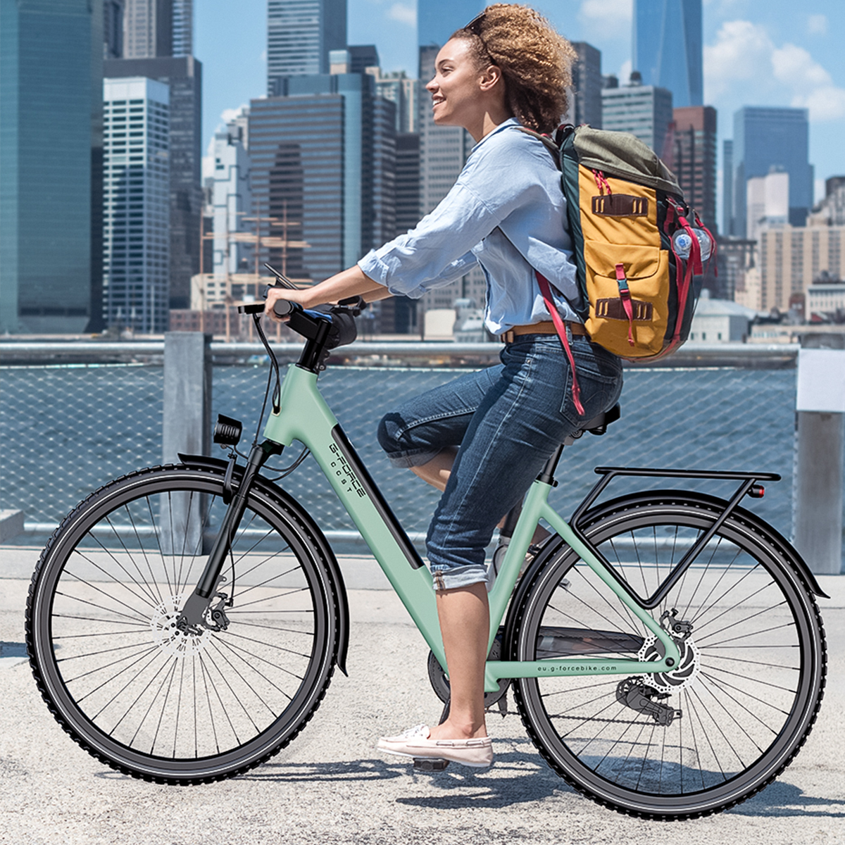 Kobieta z plecakiem jedzie miętowo-zielonym rowerem w mieście z drapaczami chmur.