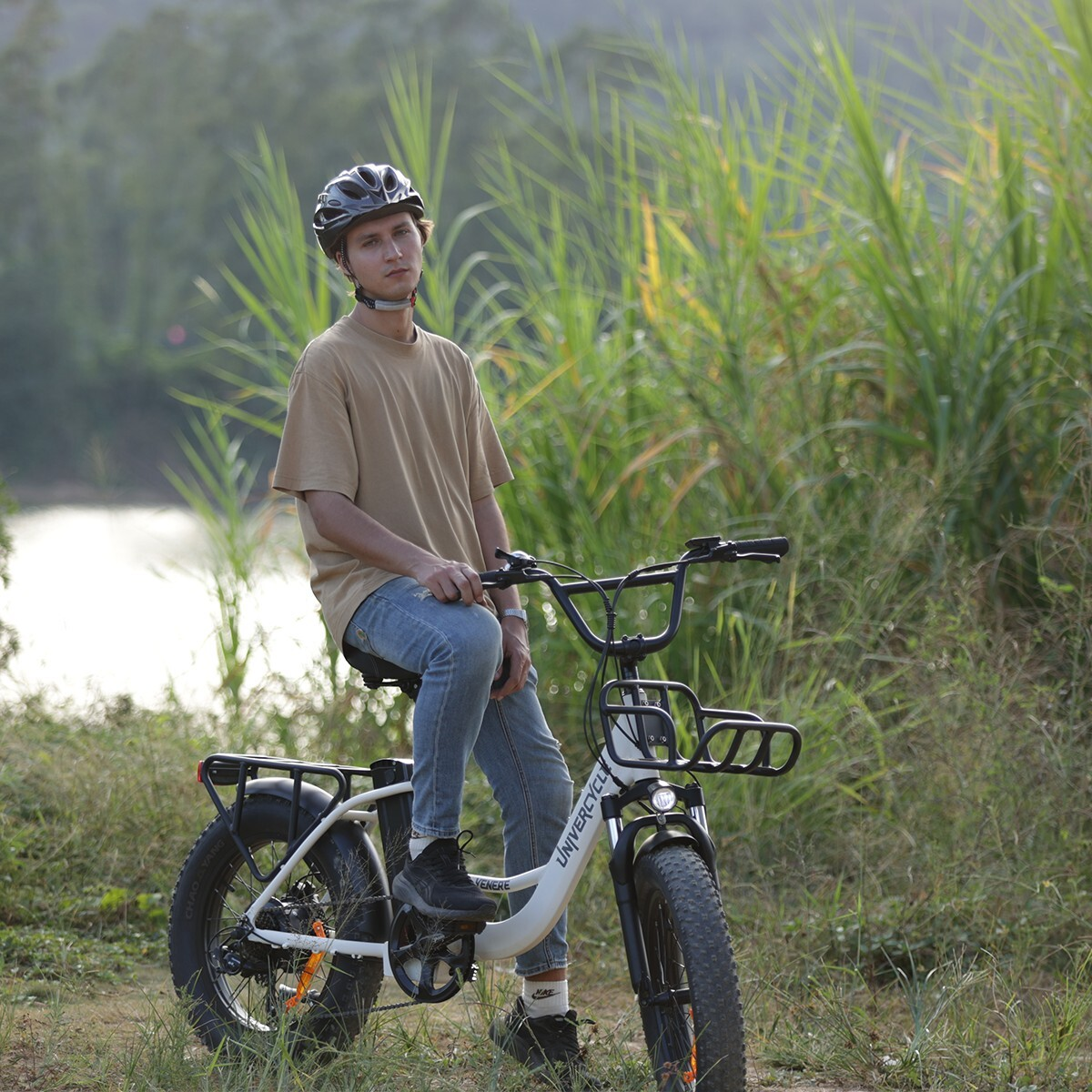 Mężczyzna w kasku siedzi na białym rowerze elektrycznym na zewnątrz, otoczony trawą.