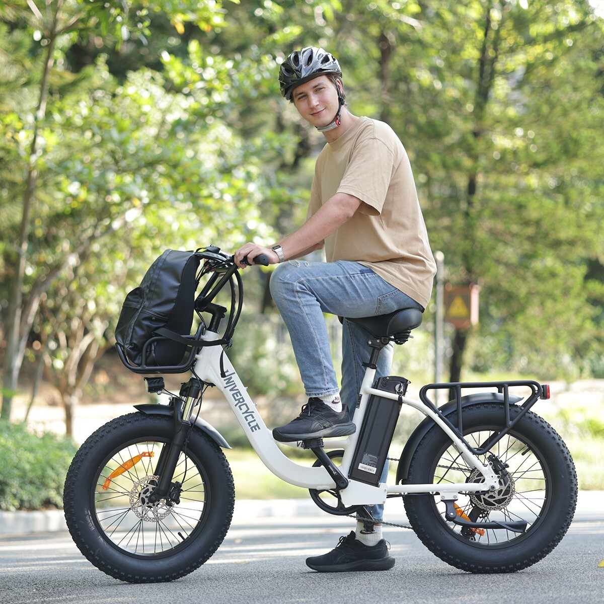 Mężczyzna w kasku siedzi na białym rowerze elektrycznym z grubymi oponami i torbą na kierownicy.