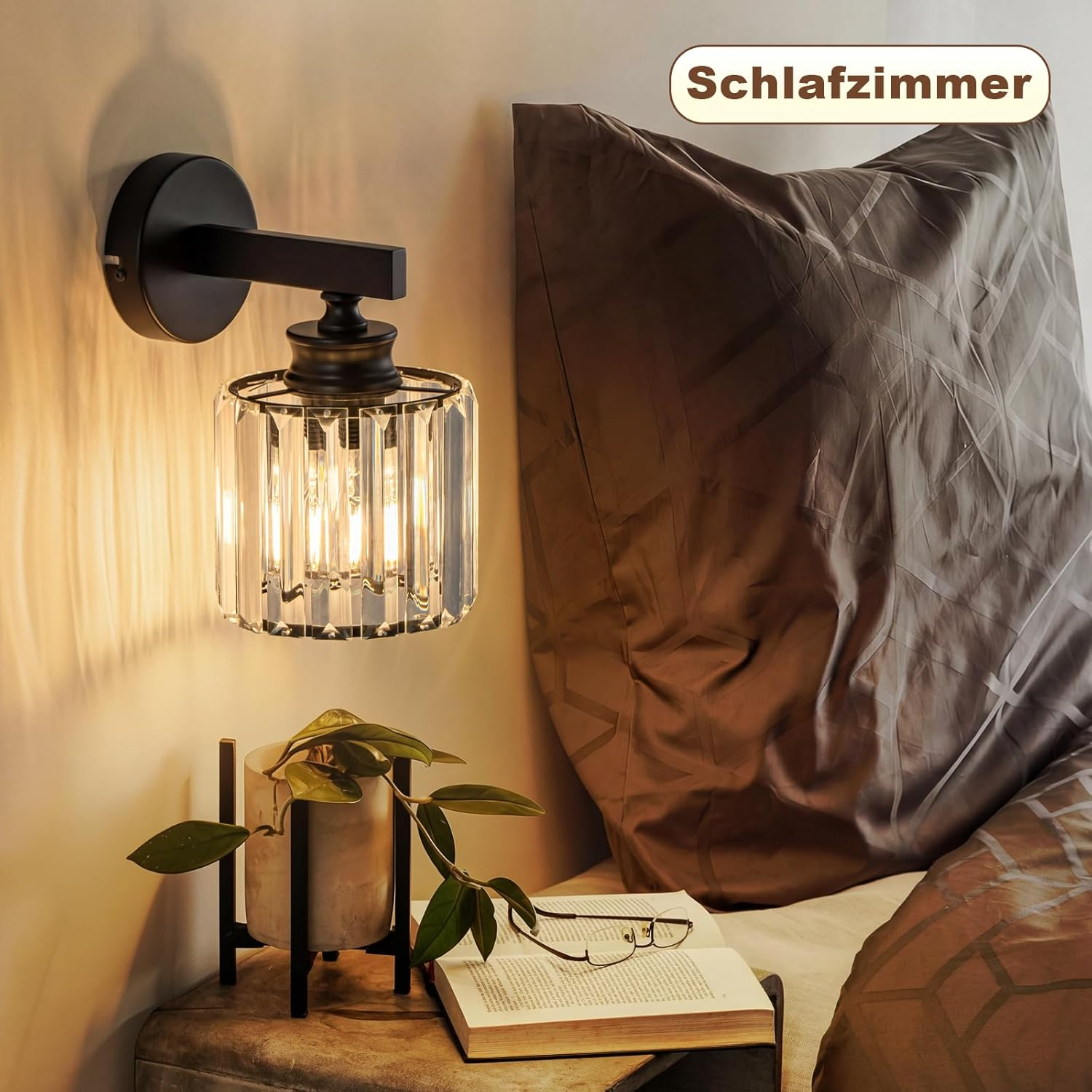 Un comodino accanto a un letto con applique in cristallo, libro e pianta.